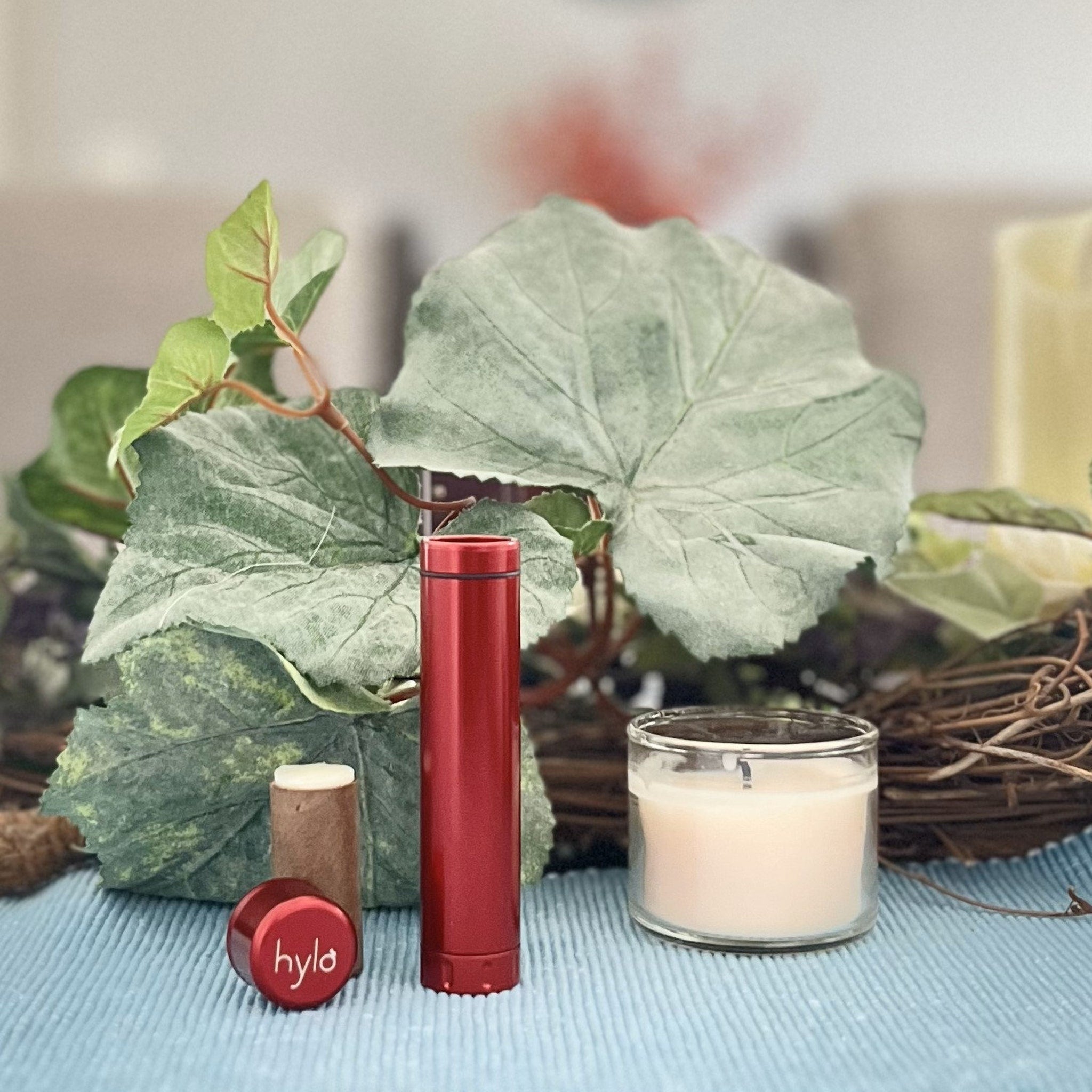 Red lipstick tube with "hylo" branding, brown lip balm, and candle on blue surface