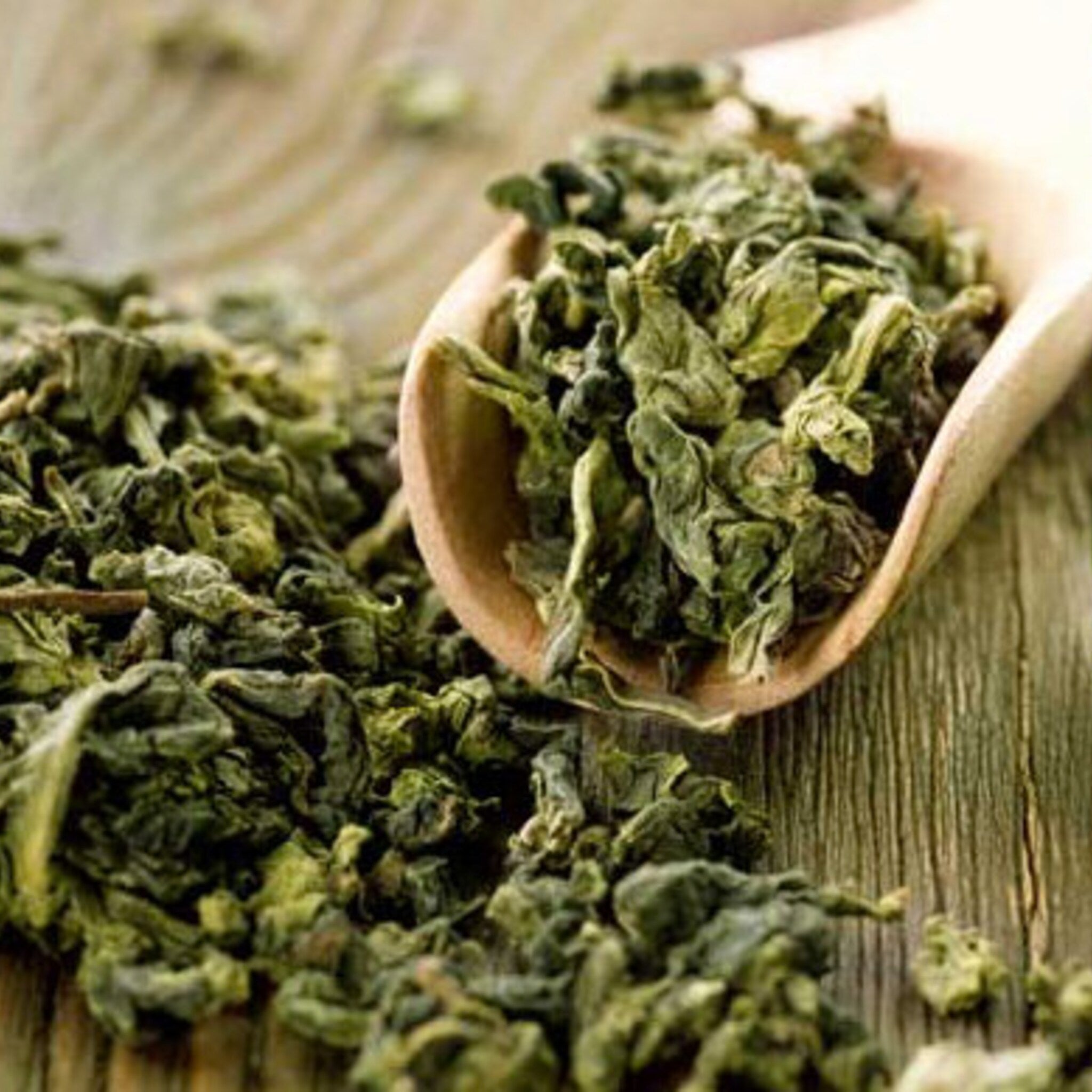 Loose leaf tea with green leaves in wooden scoop on wooden surface