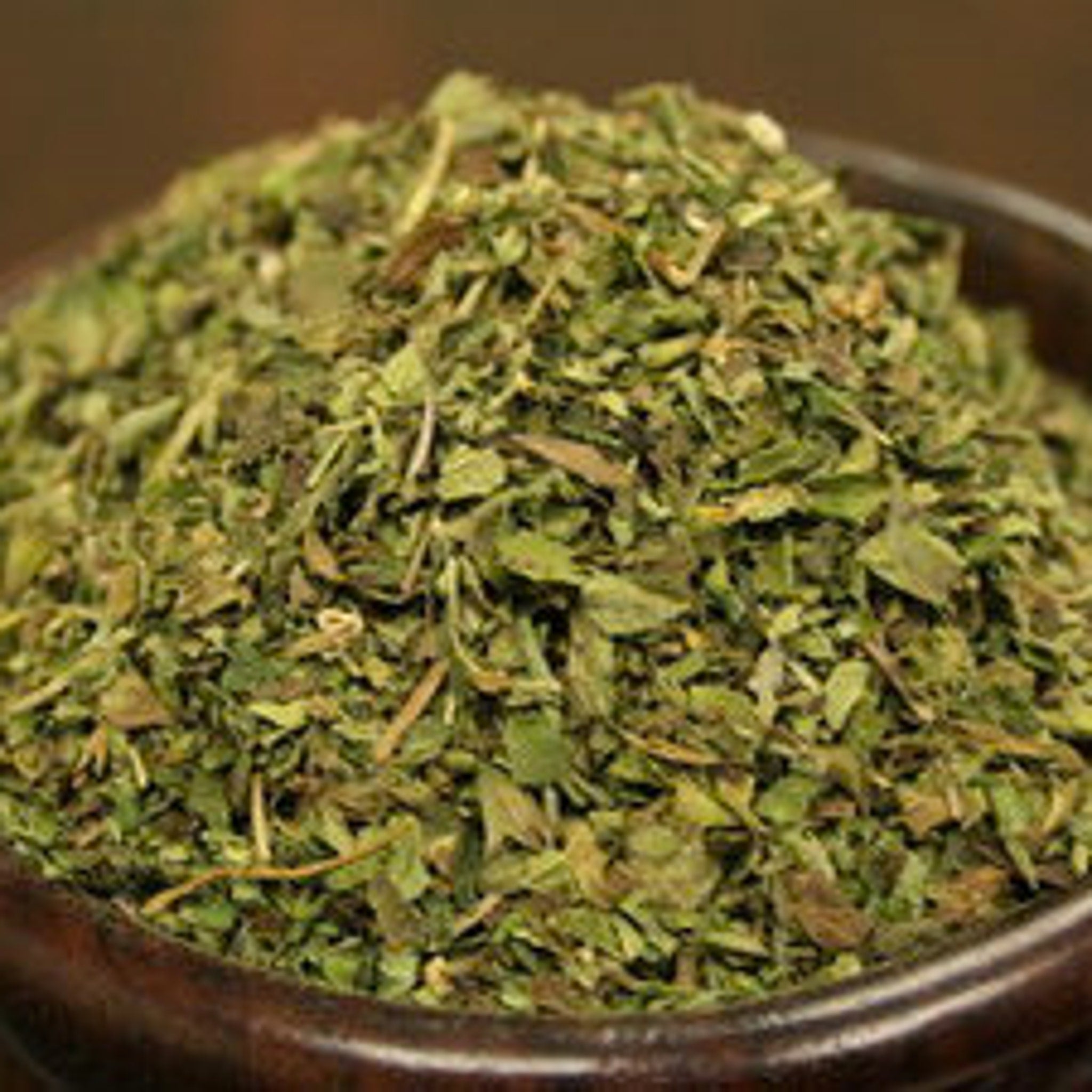 Dried herbs green and brown in a dark brown bowl, for cooking