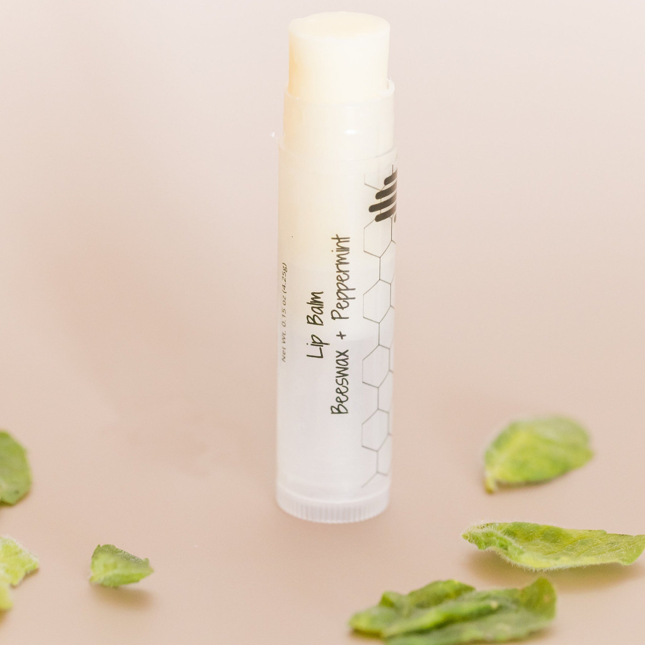 Lip balm tube with white and black text, light beige background, and green leaves around it