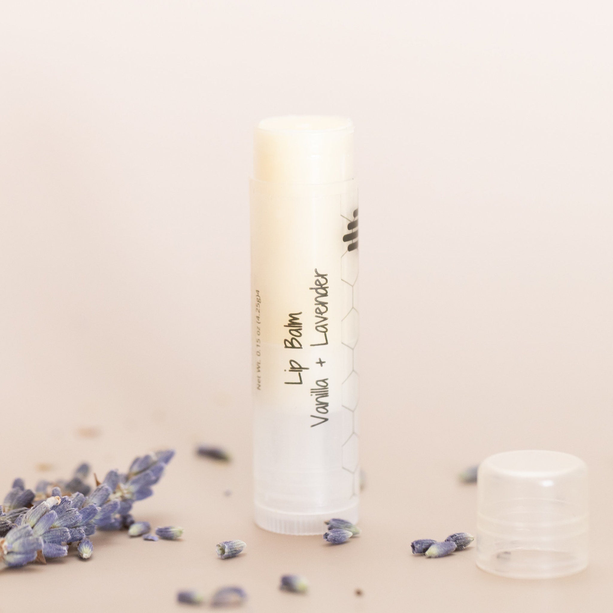 Lip balm tube with white and clear plastic, Vanilla + Lavender text, and lavender buds around it