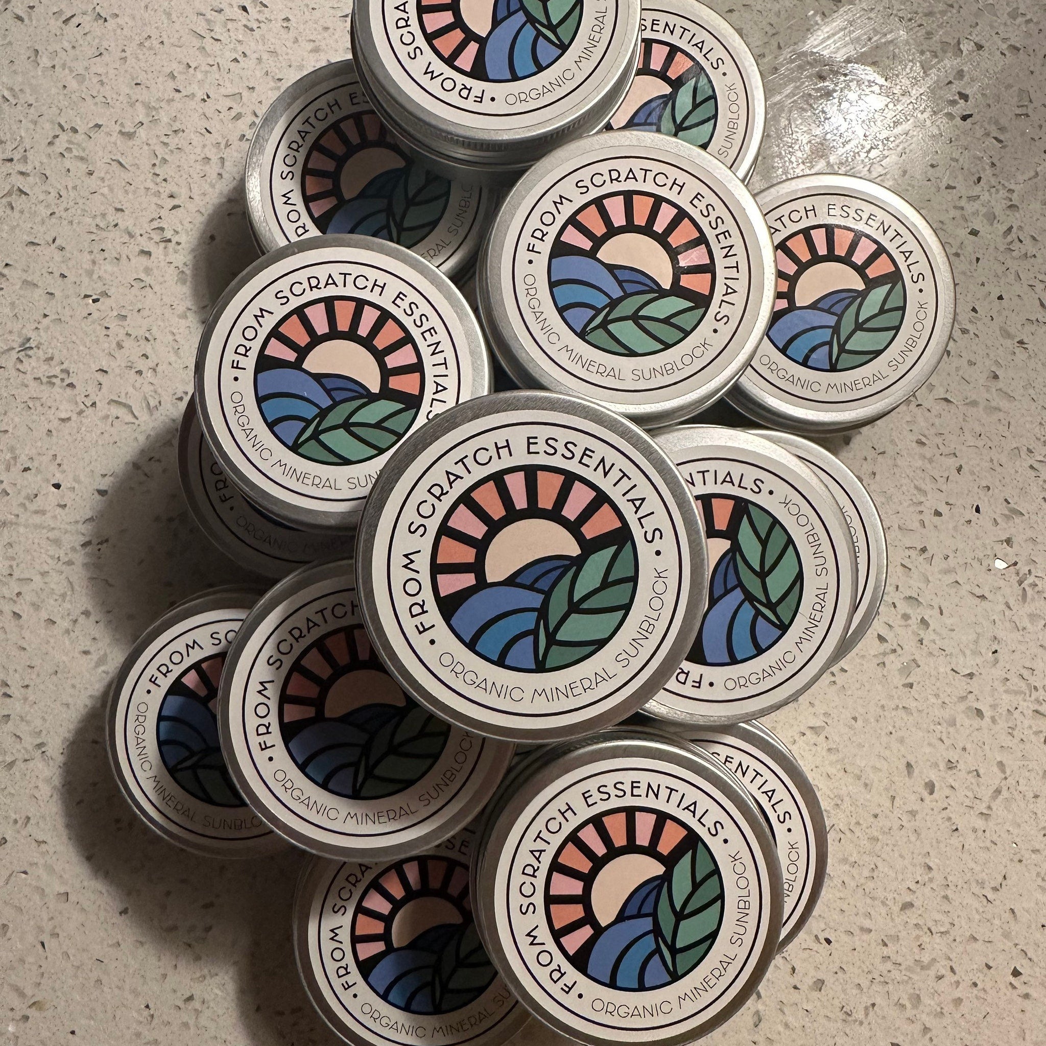 Organic mineral sunblock tins, silver metal, circular with colorful label design, stacked together.