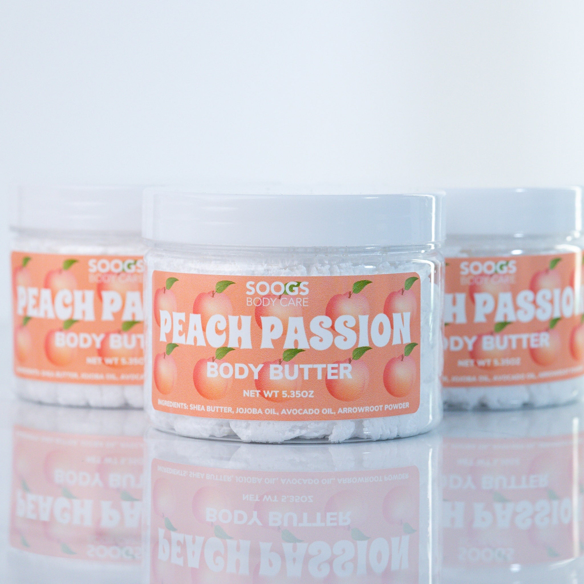 Body butter jars with white lids, peach labels, and Soogs Body Care branding