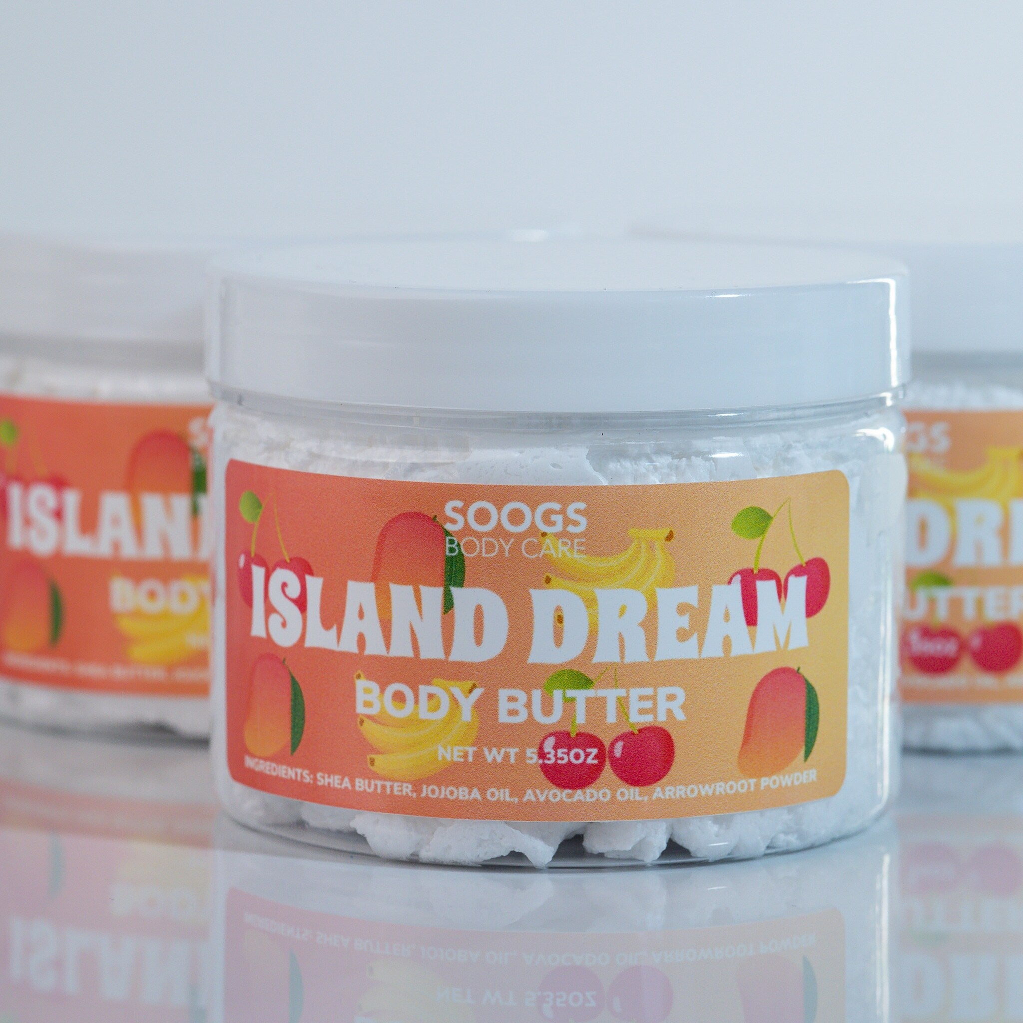Body butter jars with white contents, orange labels, and fruit graphics, Soogs brand