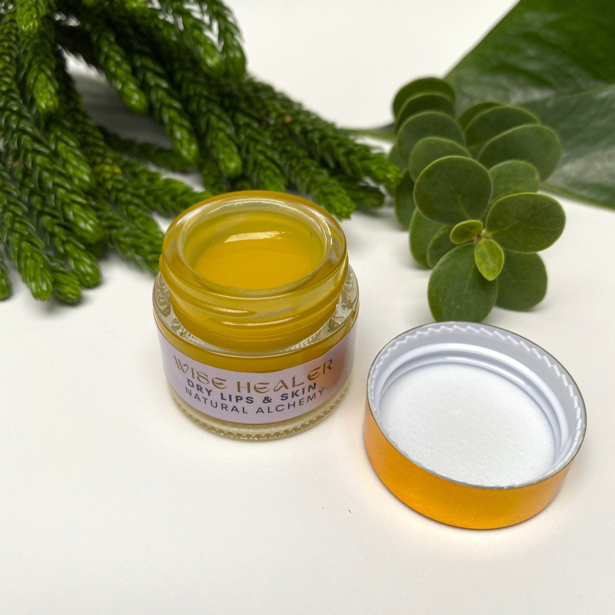 Lip balm jar with yellow balm, glass jar, and gold lid with Wise Healer label visible