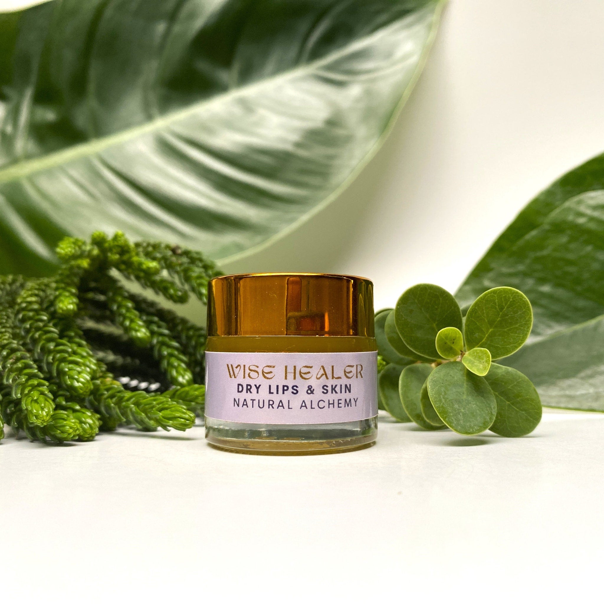 Lip balm jar with gold lid, glass container, and "Wise Healer" label on white background