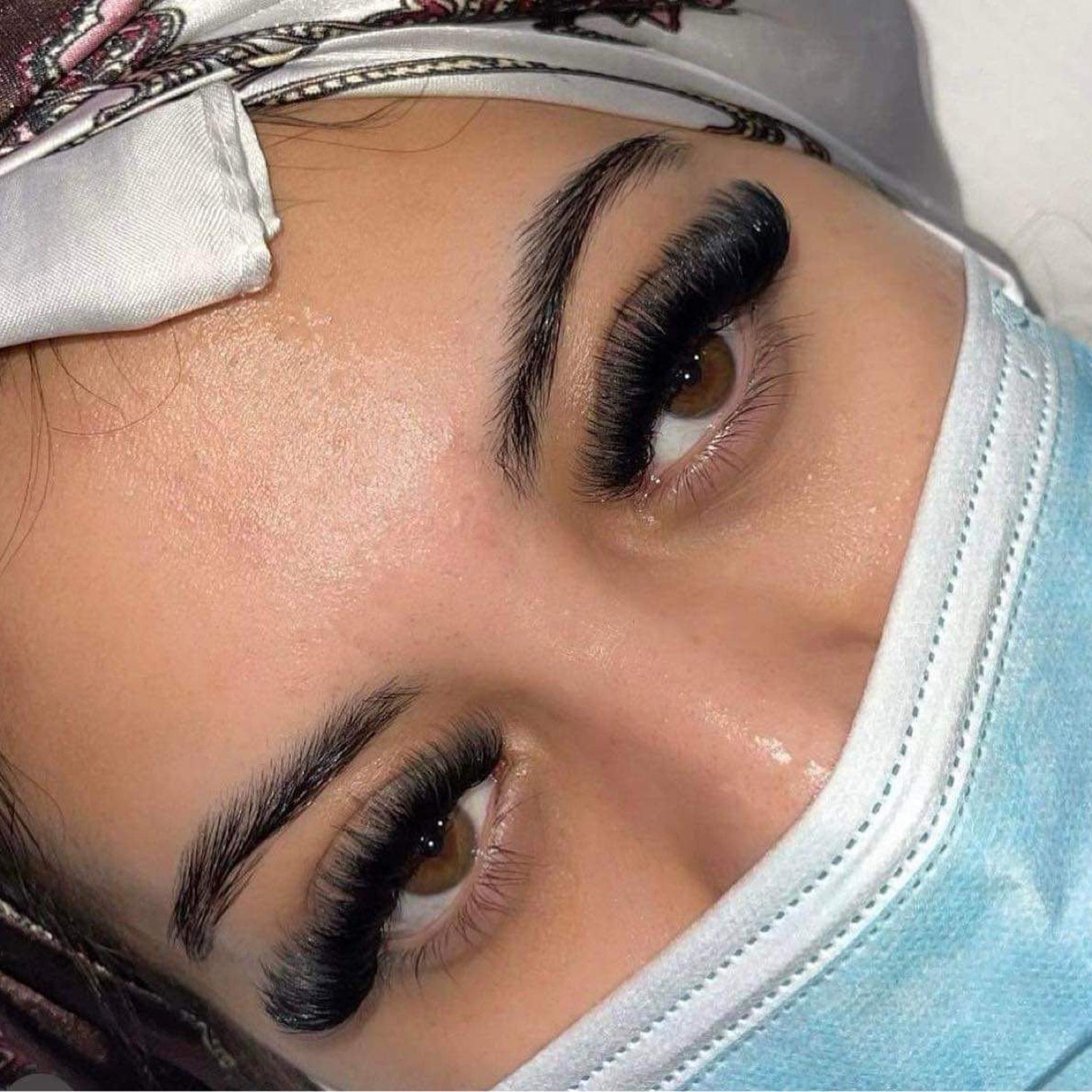 Eyelash extensions, black lashes, brown eyes, blue face mask, close-up view