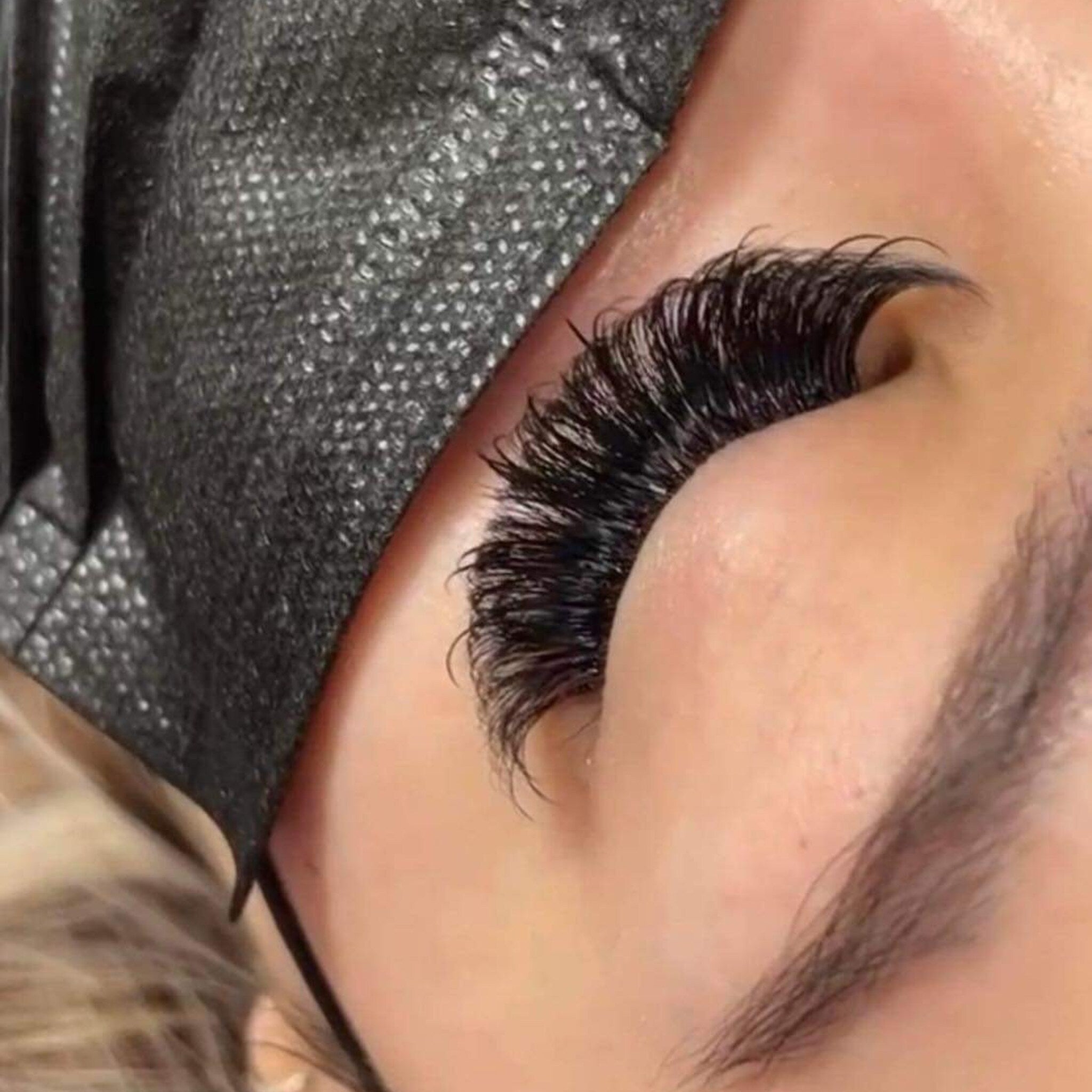 Eyelash extensions with black lashes, black mask, and skin tone background.