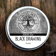 Drawing salve tin with silver rim, black and white label, and Woodland Herbal branding