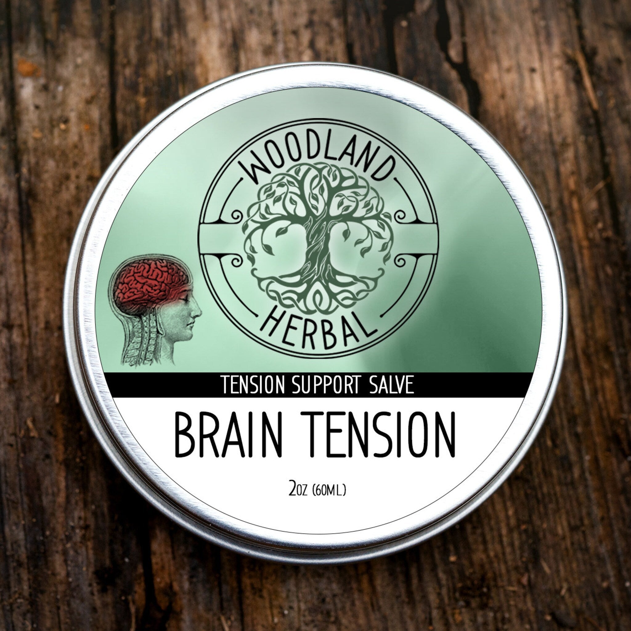 Brain tension salve tin with silver metal rim, green label, and Woodland Herbal text