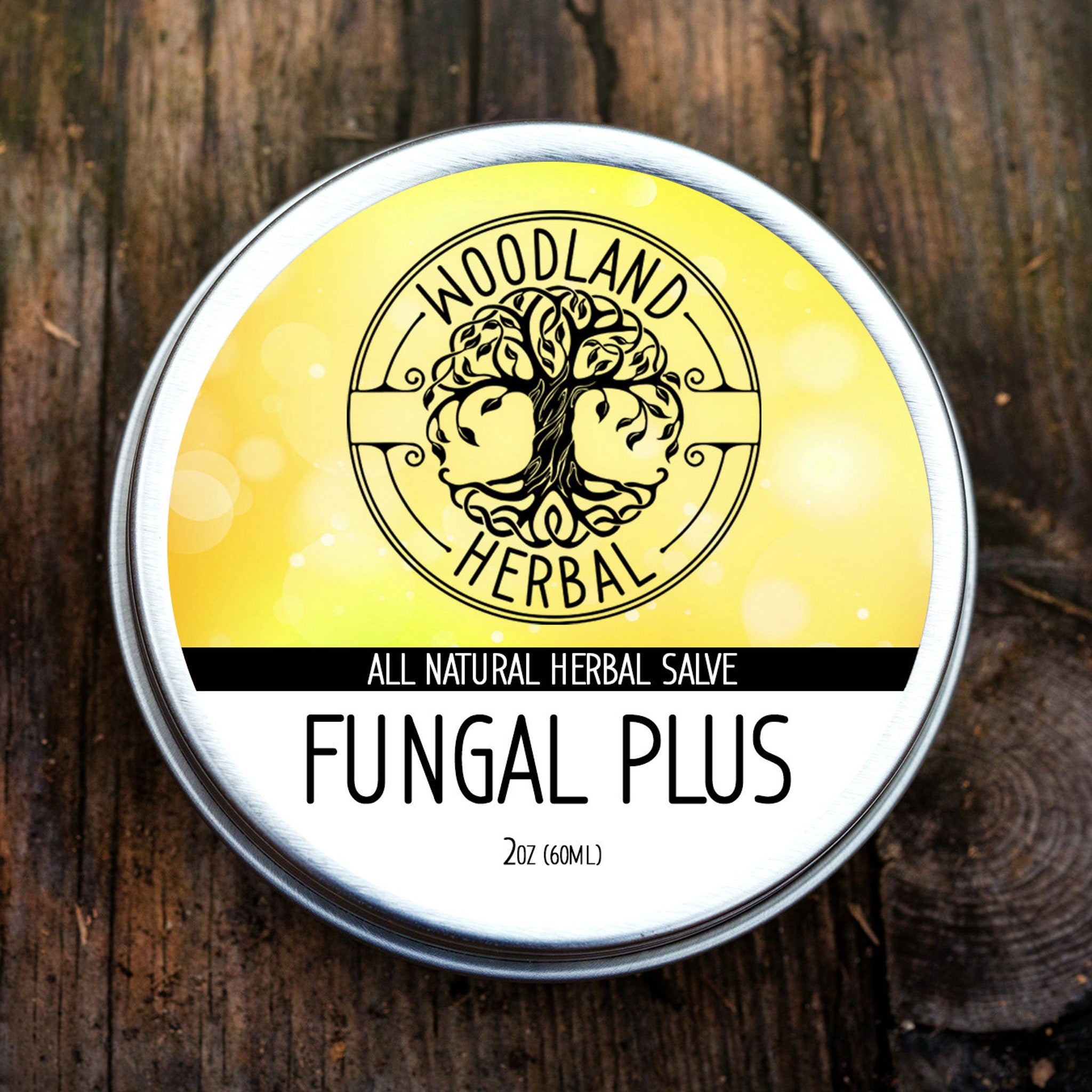 Herbal salve tin with yellow and white label, black text, and Woodland Herbal logo on wooden surface