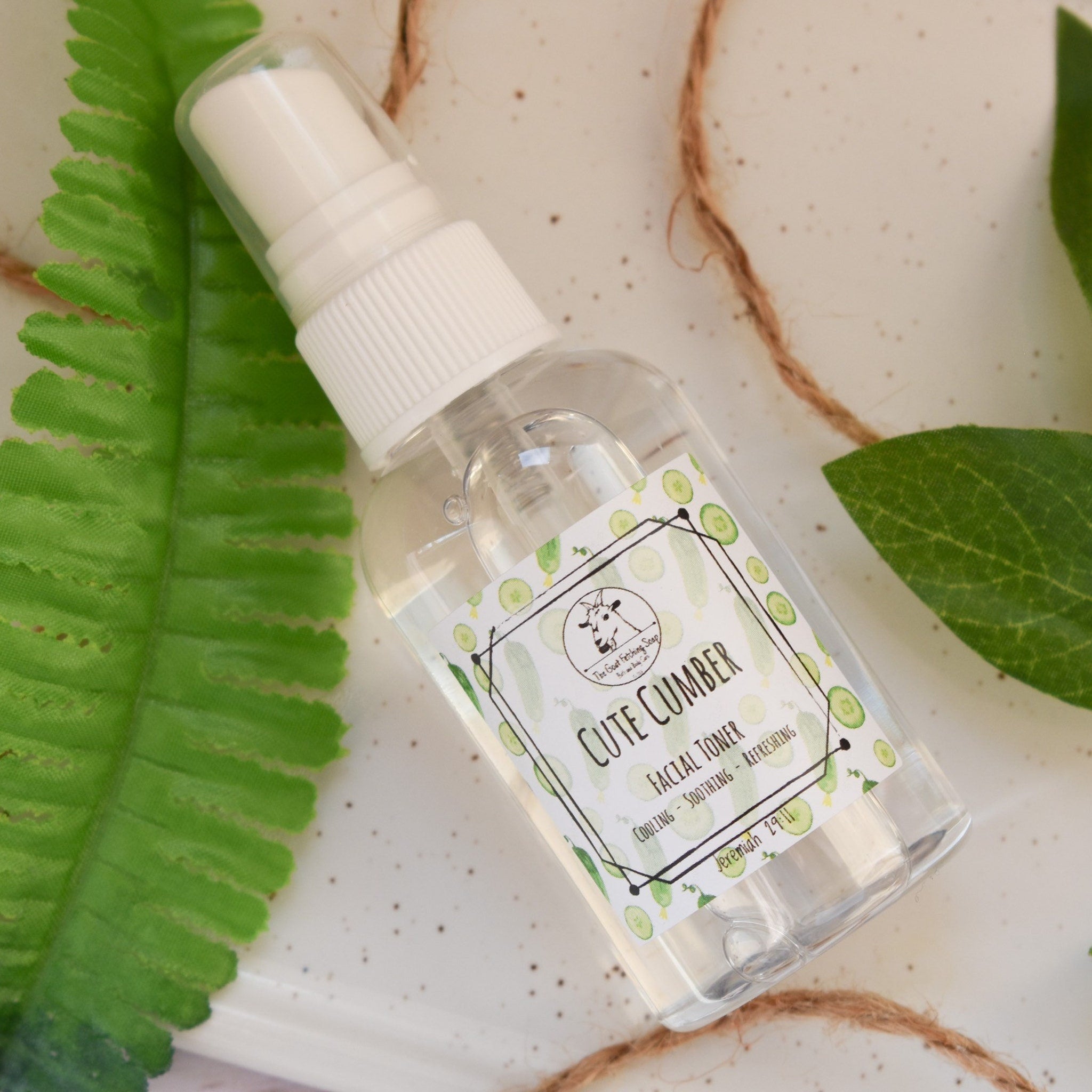Facial toner spray bottle with clear liquid and white cap, labeled "Cute CUMBER" with cucumber illustrations and green leaves around it