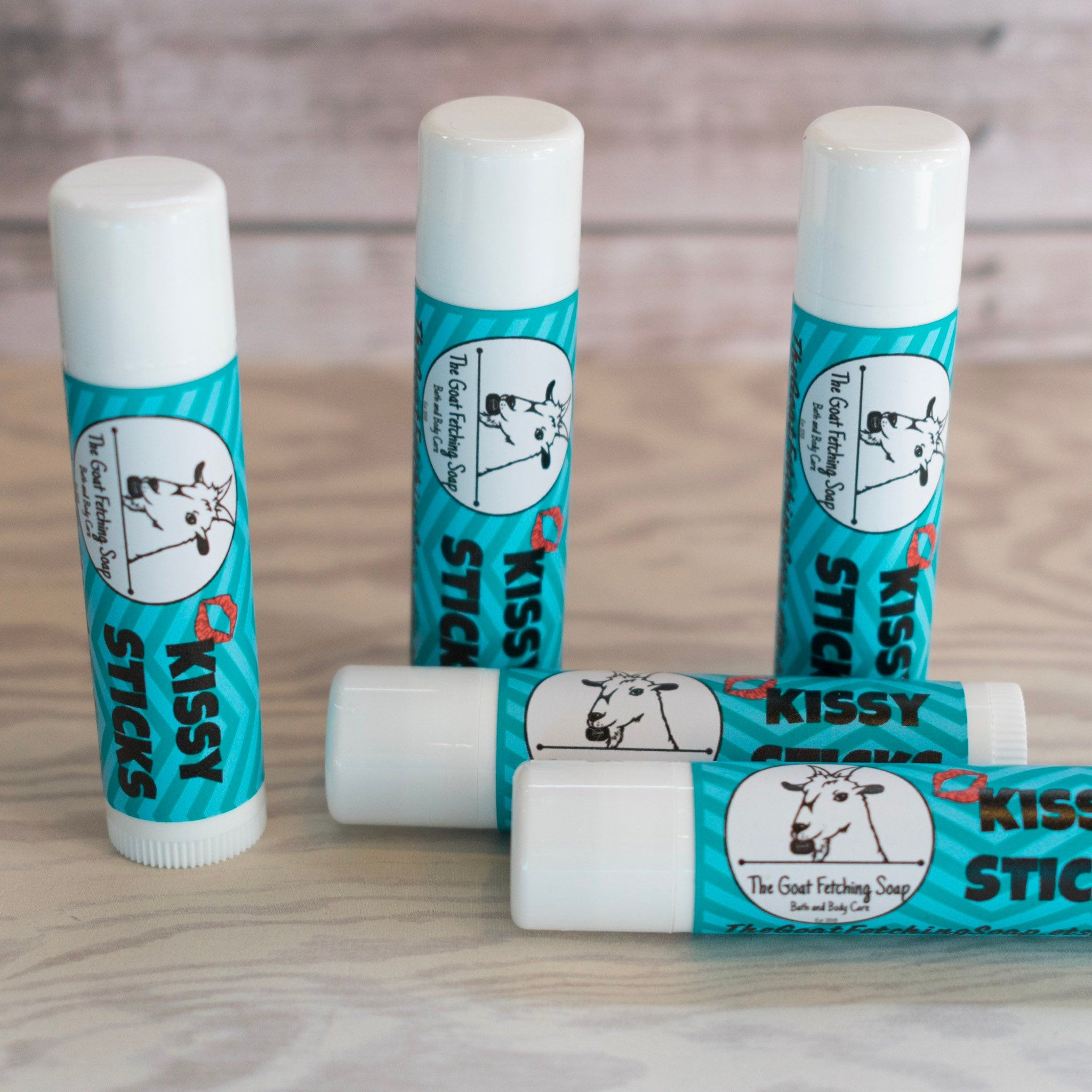 Lip balm tubes, white and teal striped, with "Kissy Sticks" and goat logo visible