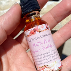Rosehip oil bottle with floral label, amber liquid, and black cap held in hand by Addictive Cosmetics