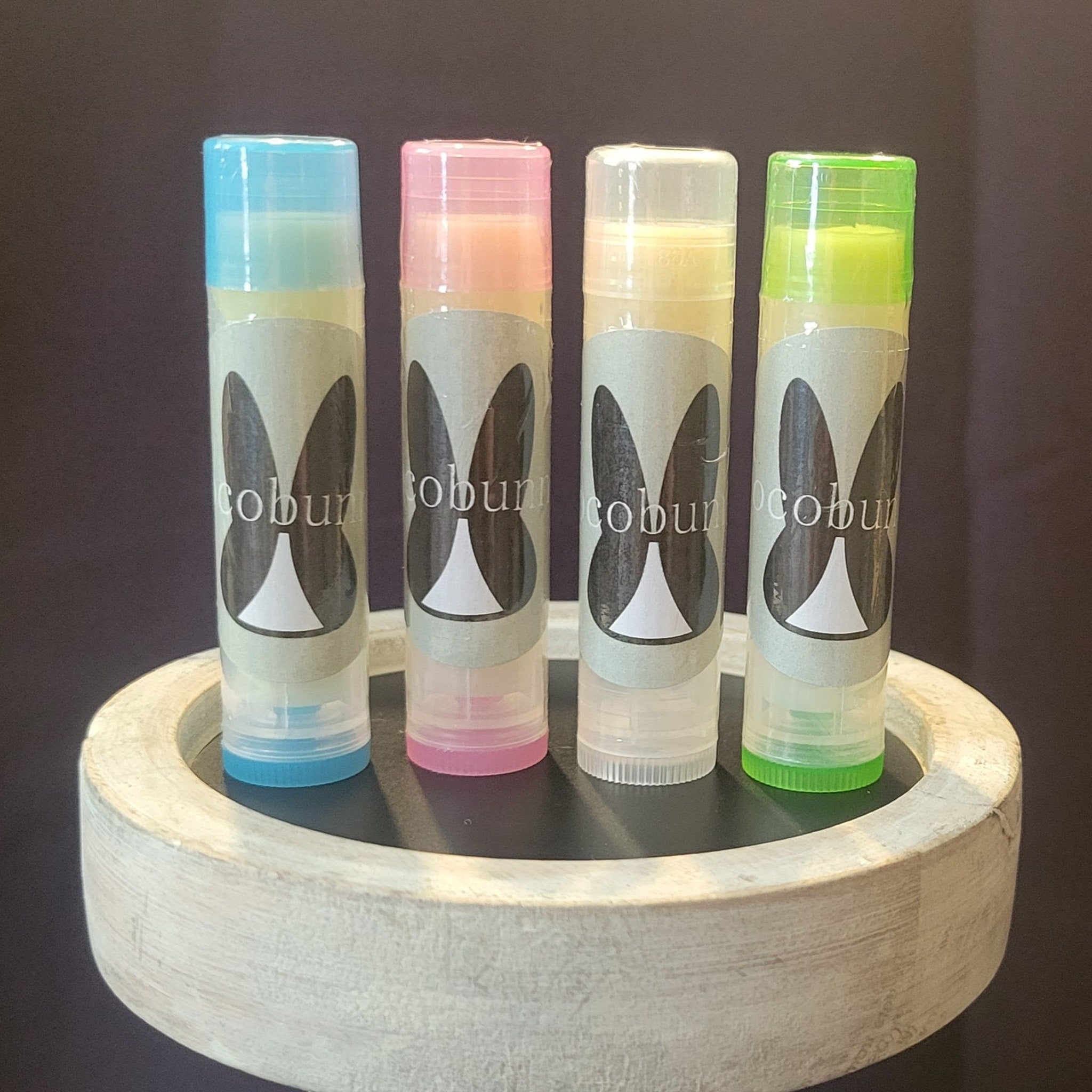 Lip balms, four tubes with colorful caps, CocoBunny logo, on a white wooden tray