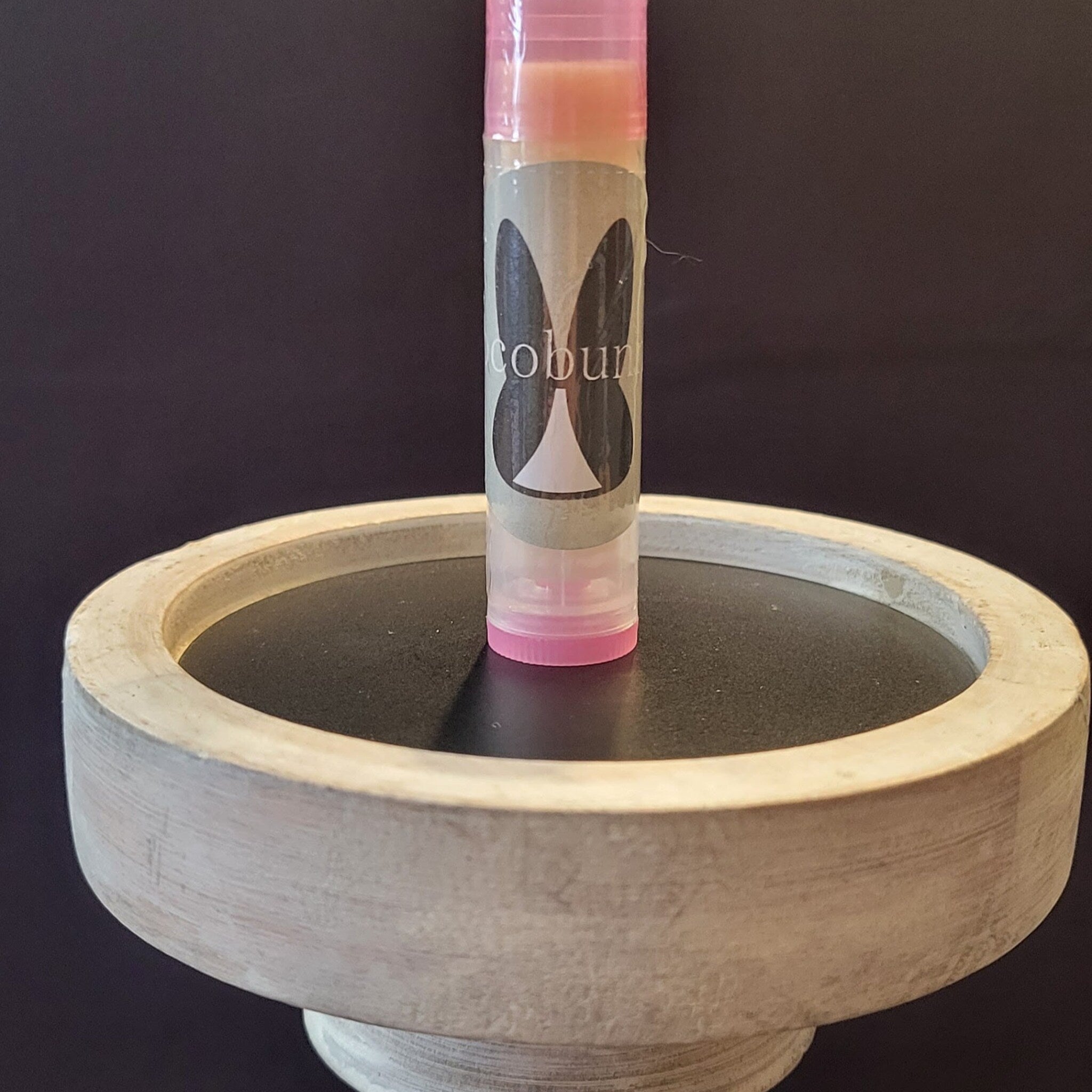 Lip balm tube with pink cap, "cobun" label, and standing on a round wooden display