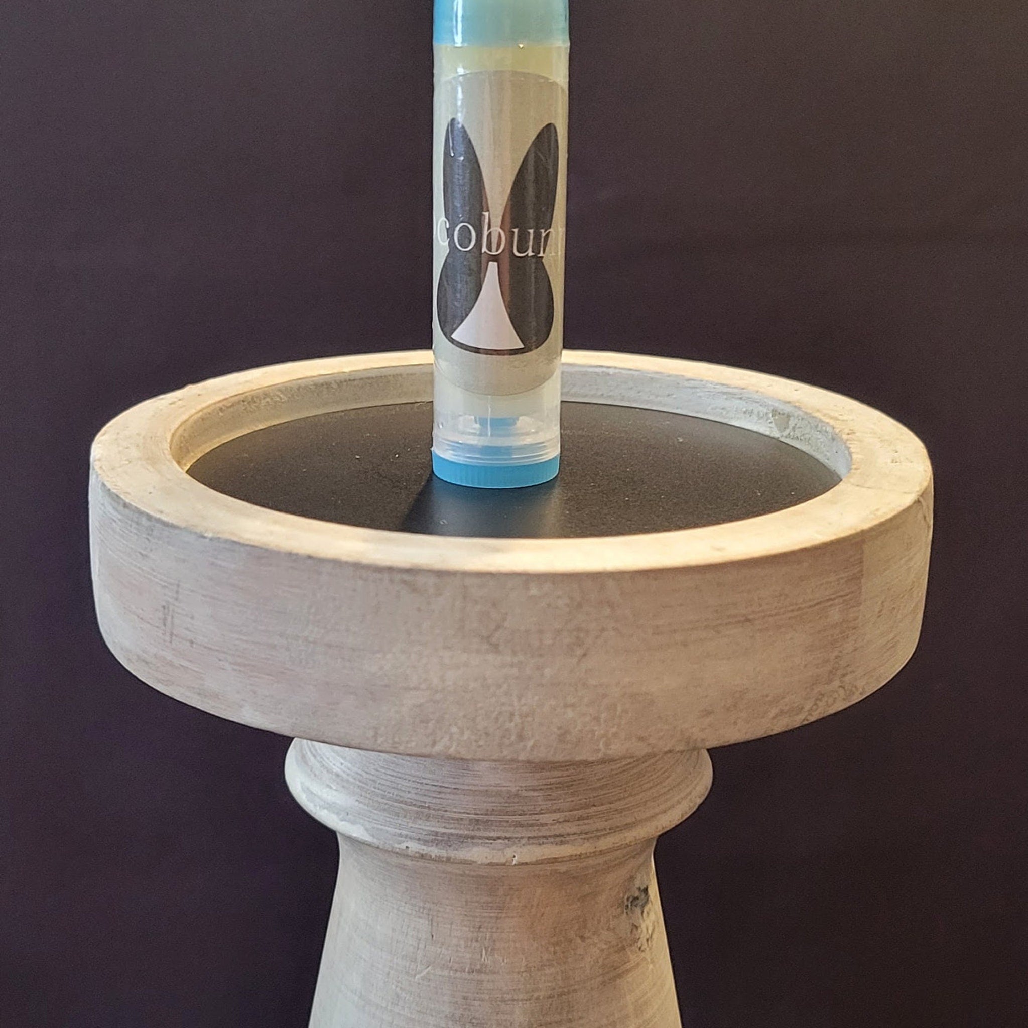 Lip balm tube with "cobun" label, light blue accents, and a wooden stand with dark top.