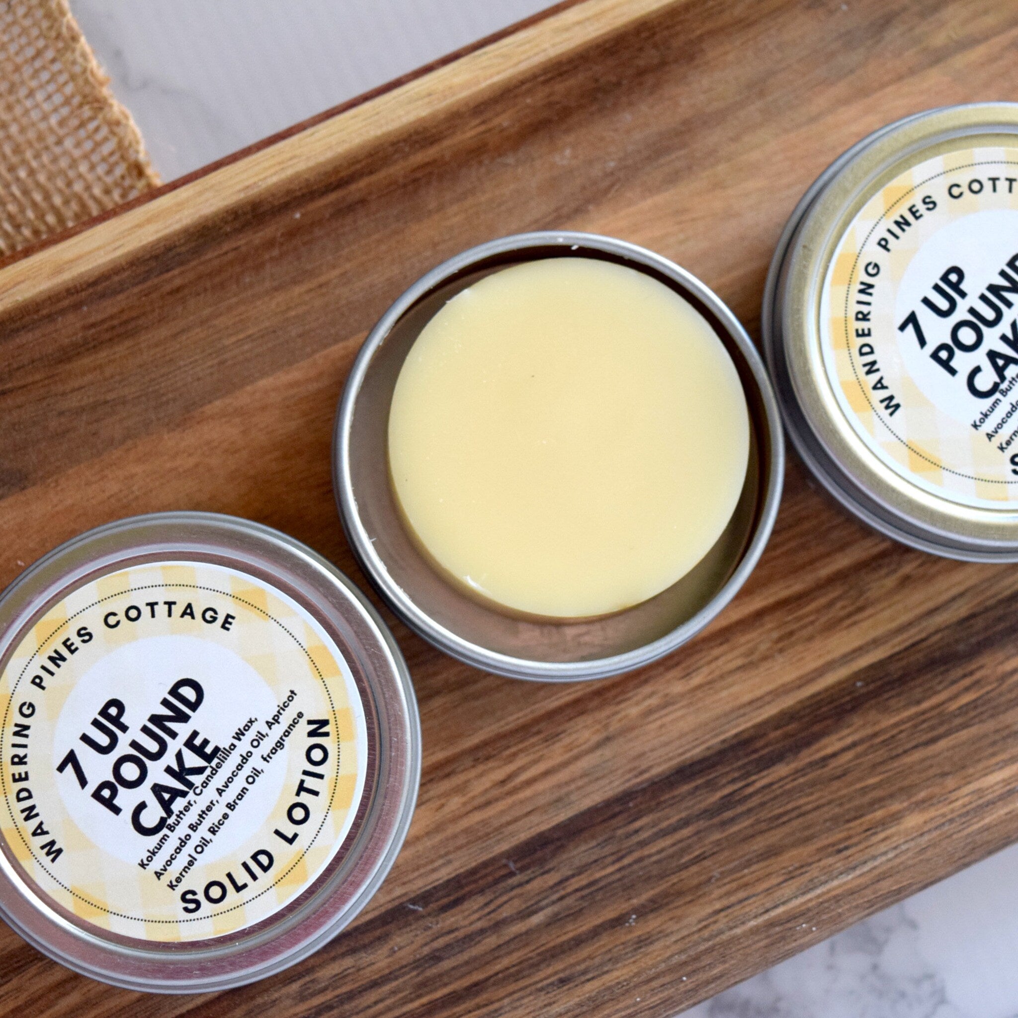 Solid lotion in round metal tins with yellow and white labels on wooden tray