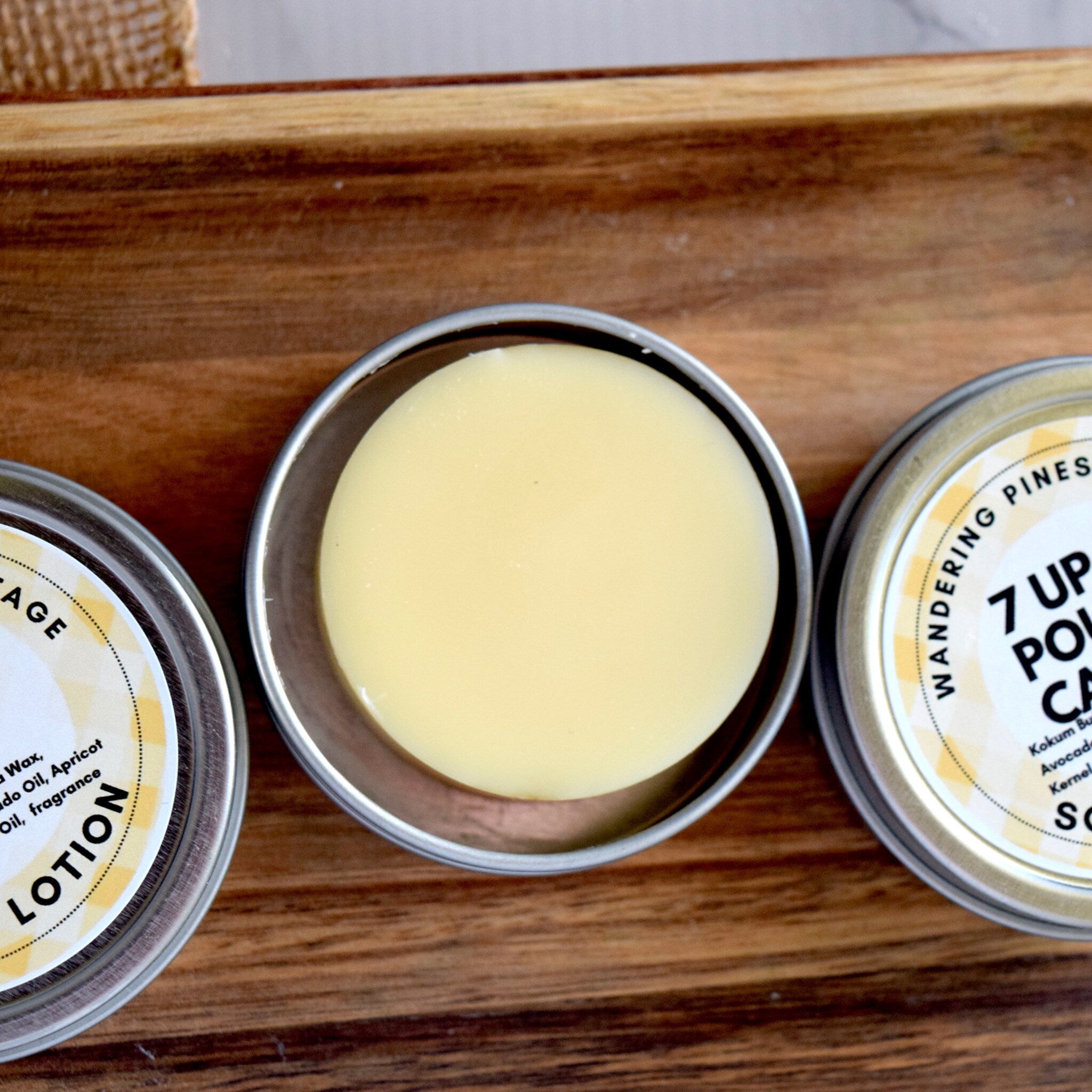 Lotion tins with yellow balm, silver metal containers, and wooden tray background