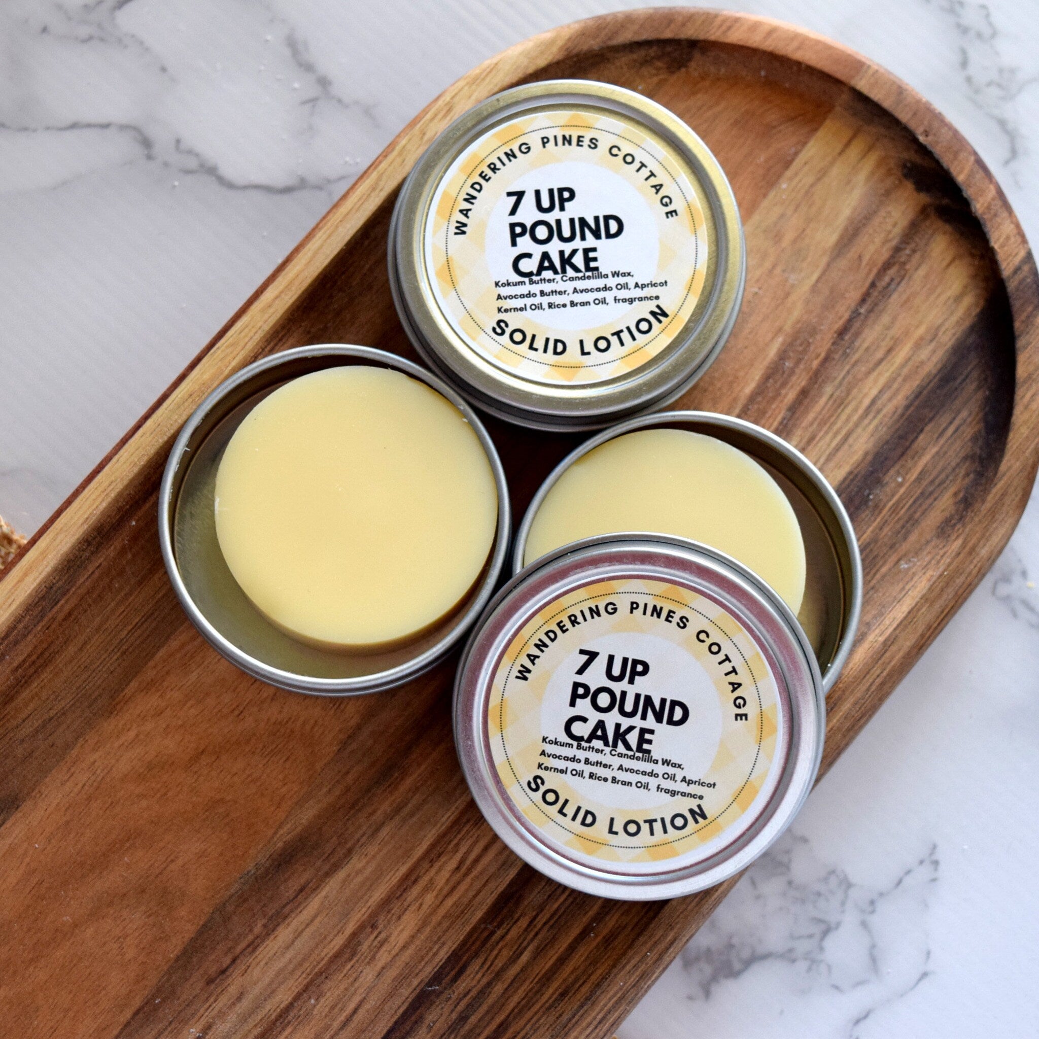 Solid lotion in silver tins with yellow product and brand text on a wooden tray