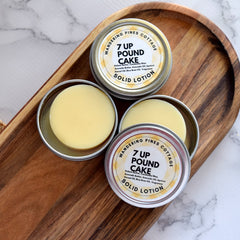 Solid lotion in silver tins with yellow product and brand text on a wooden tray