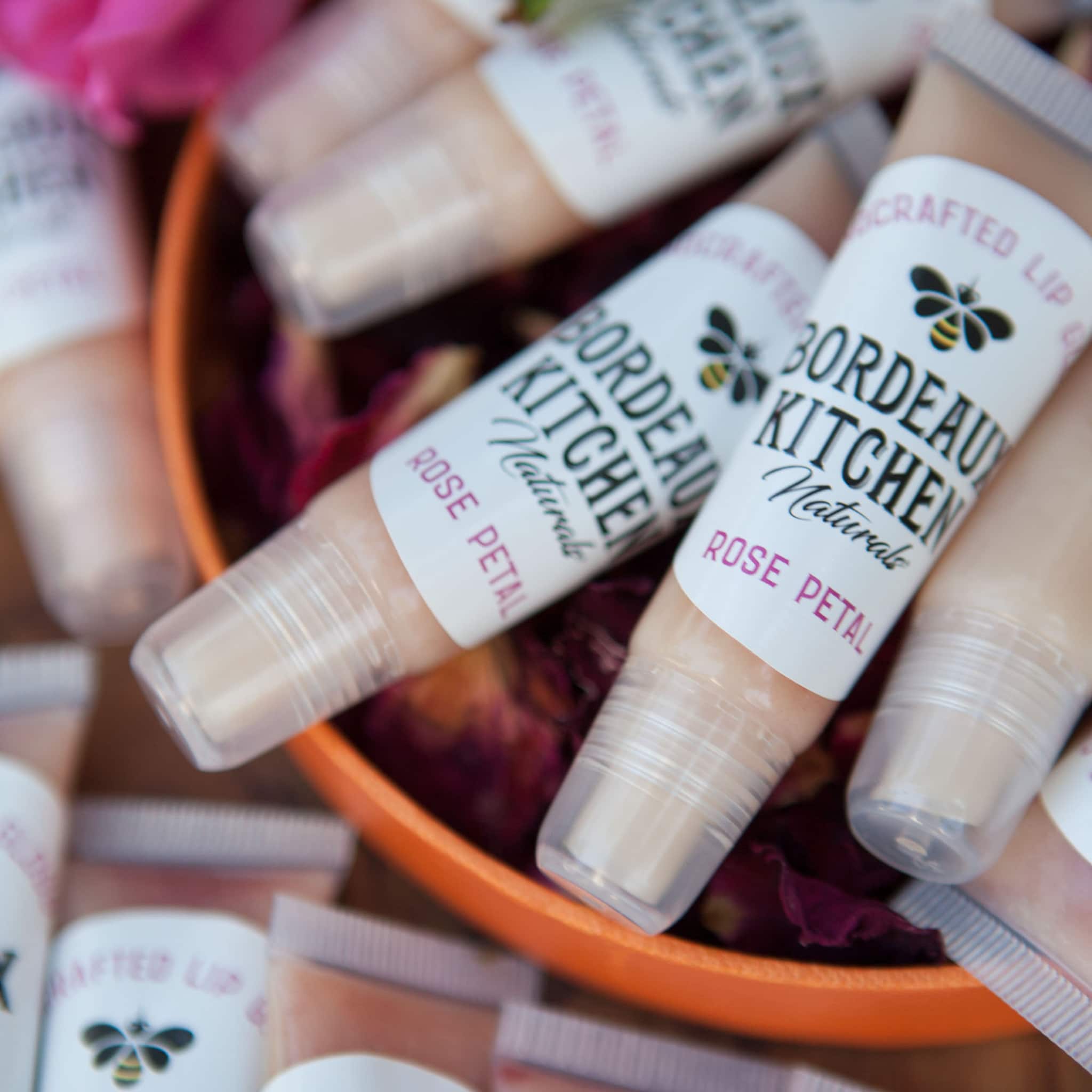 Lip gloss tubes with white labels, clear caps, and "Bordeaux Kitchen Naturals" text, in orange bowl