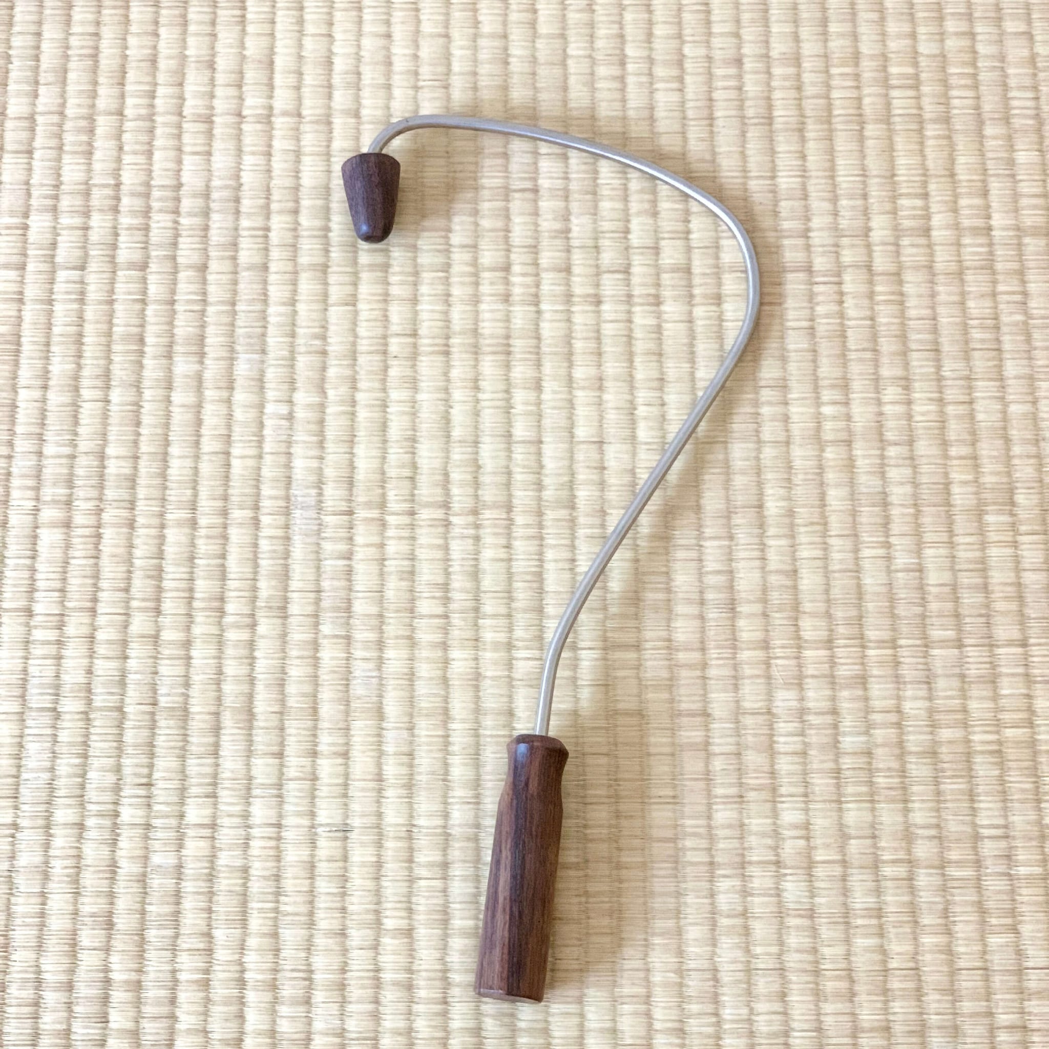 Neck massager tool with dark wood handle and head, silver metal arm, on woven mat