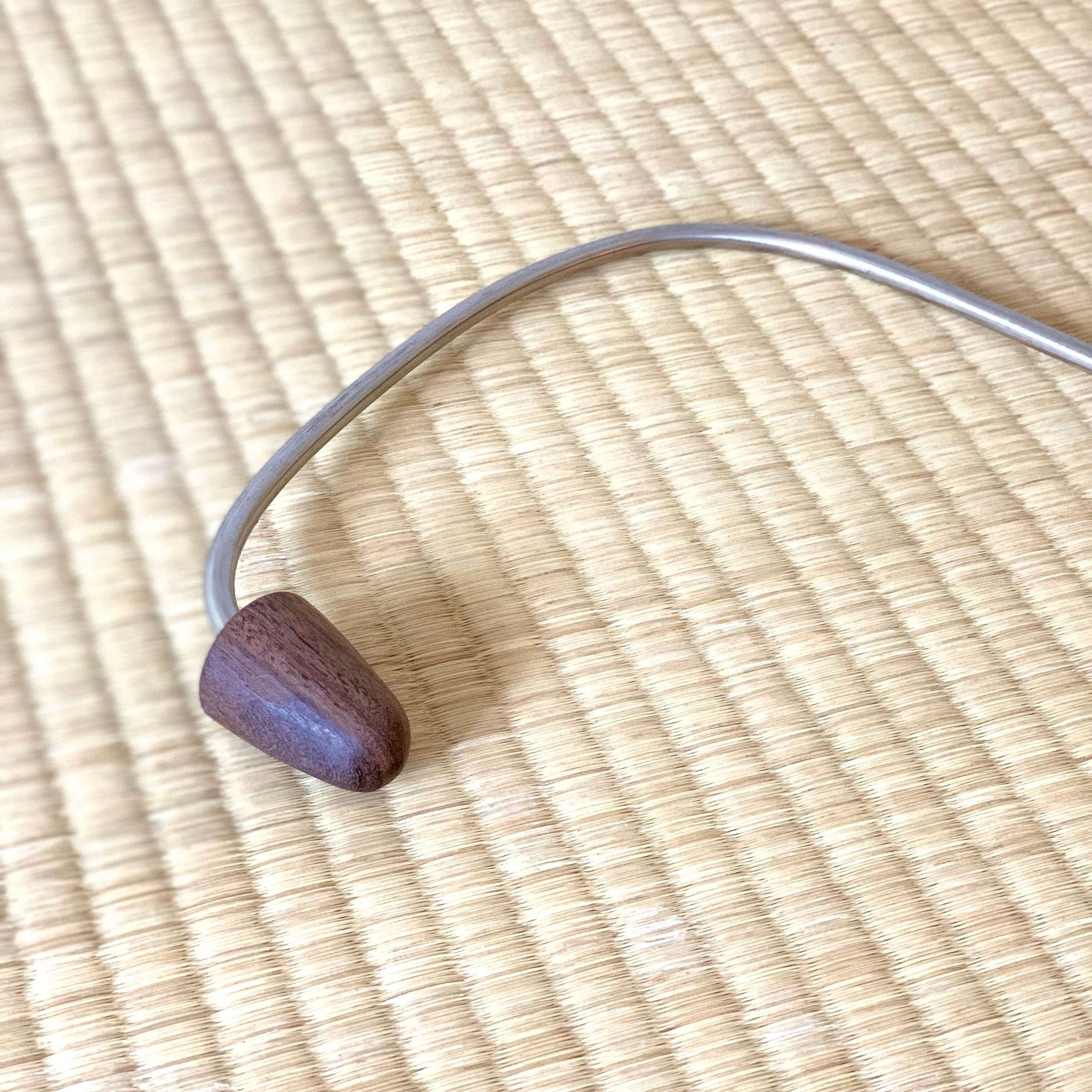 Metal and wood massage tool with curved metal and dark wood head on woven mat background