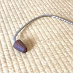 Metal and wood massage tool with curved metal and dark wood head on woven mat background