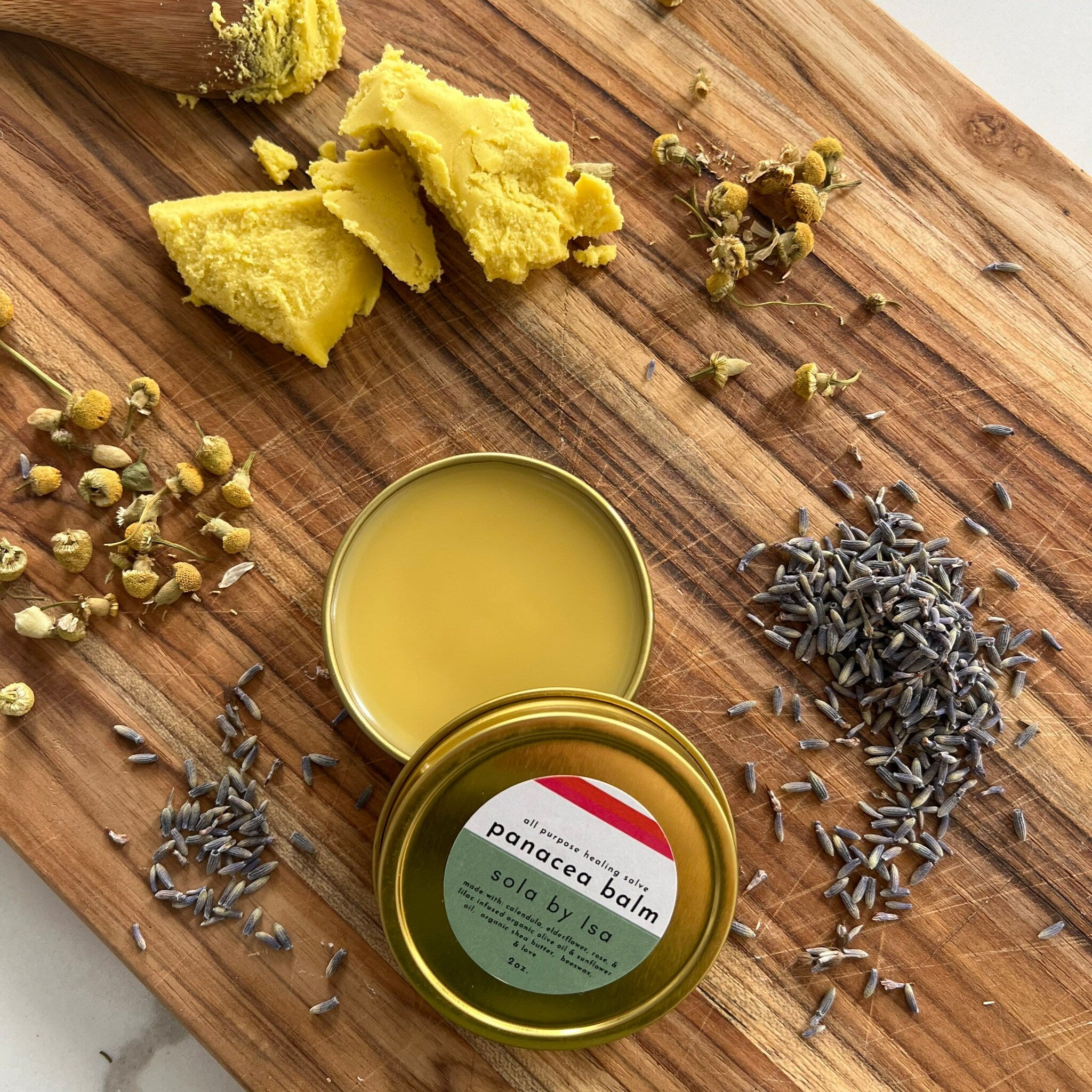 Healing salve in gold tin, yellow balm, with dried lavender and sola by Isa label on wood surface
