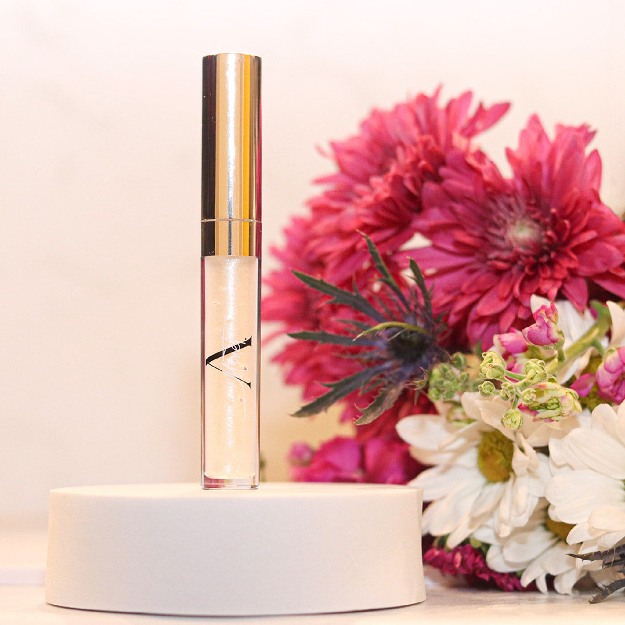 Lip gloss tube with gold cap and clear tube, A.Monét branding visible, on white stand