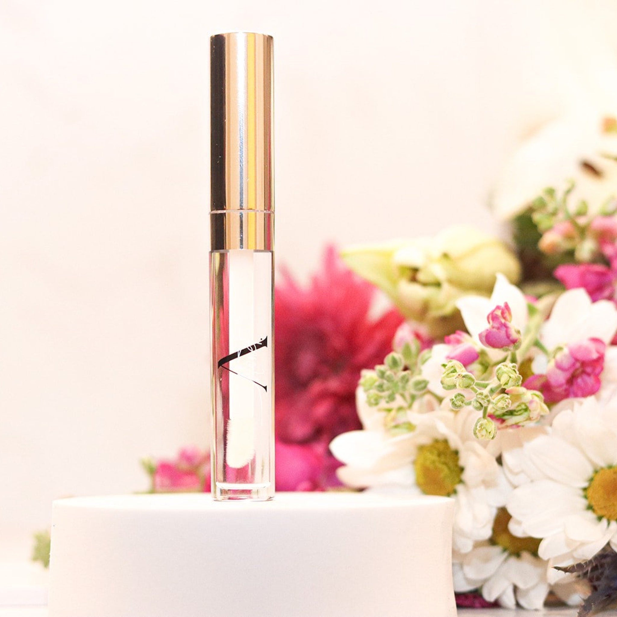 Lip gloss tube with clear gloss, gold cap, and A.Monét branding on white stand