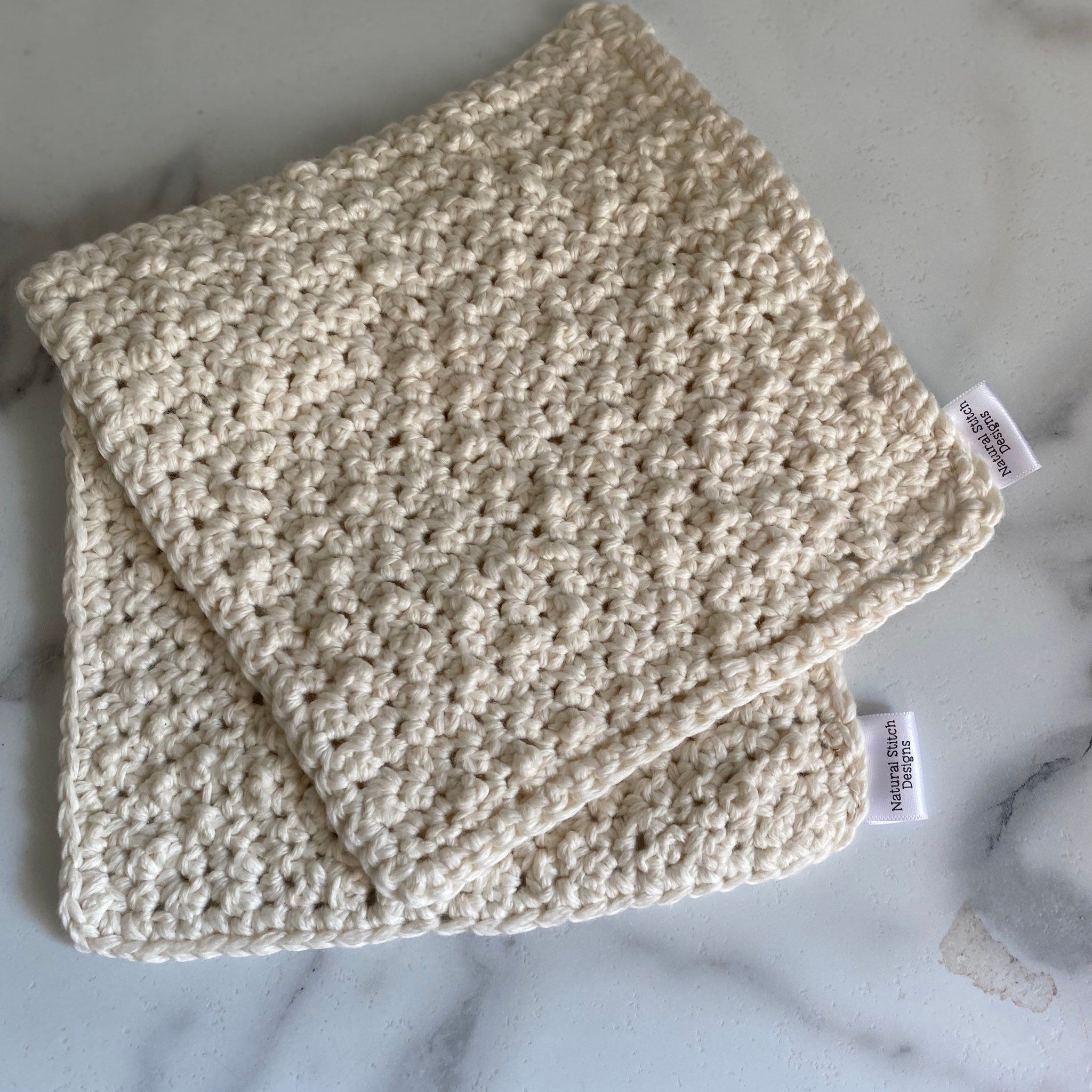 Crocheted washcloths in off-white, handmade, with Natural Stitch Designs label visible