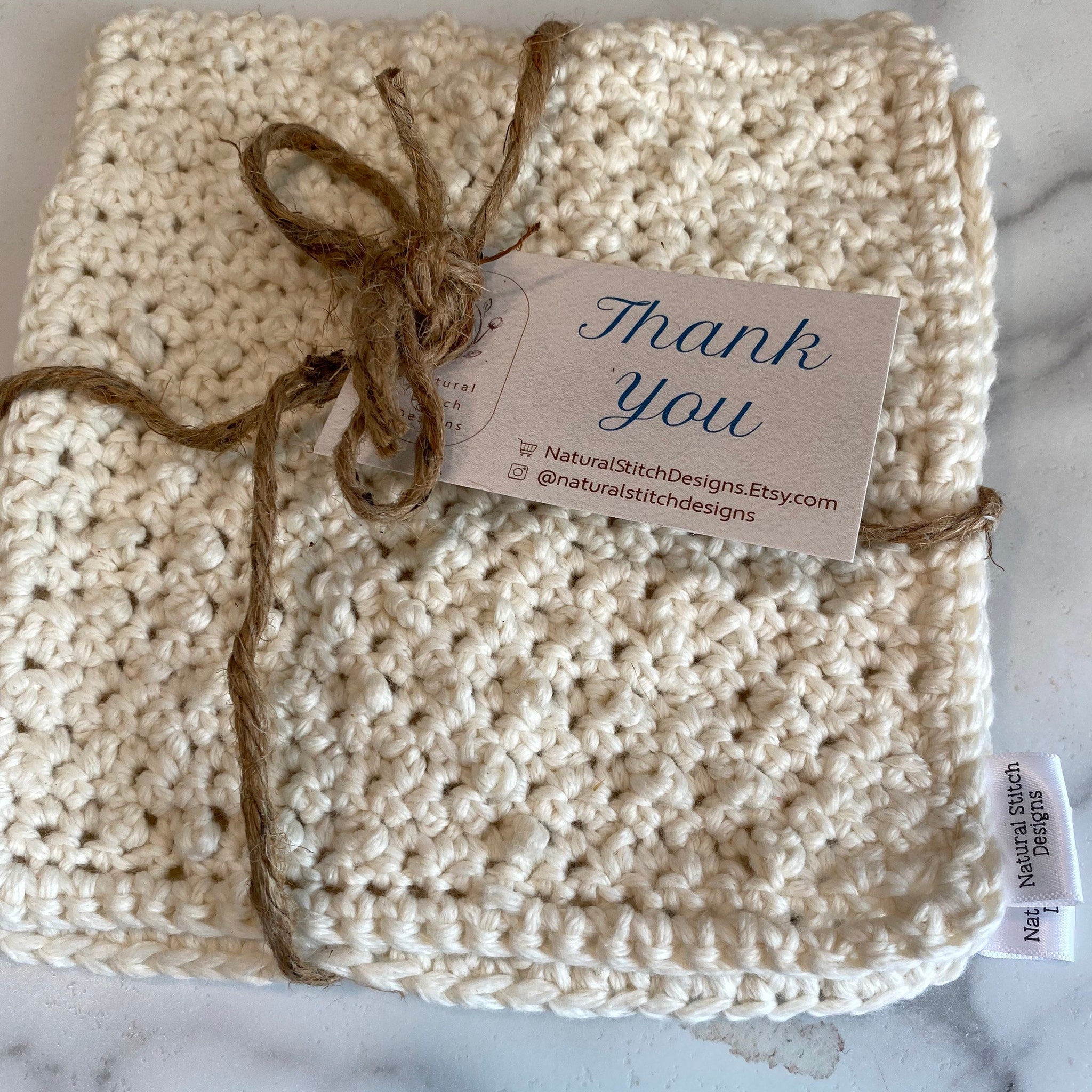 Crocheted item, cream-colored material with visible stitch pattern, tied with twine, Natural Stitch Designs tag