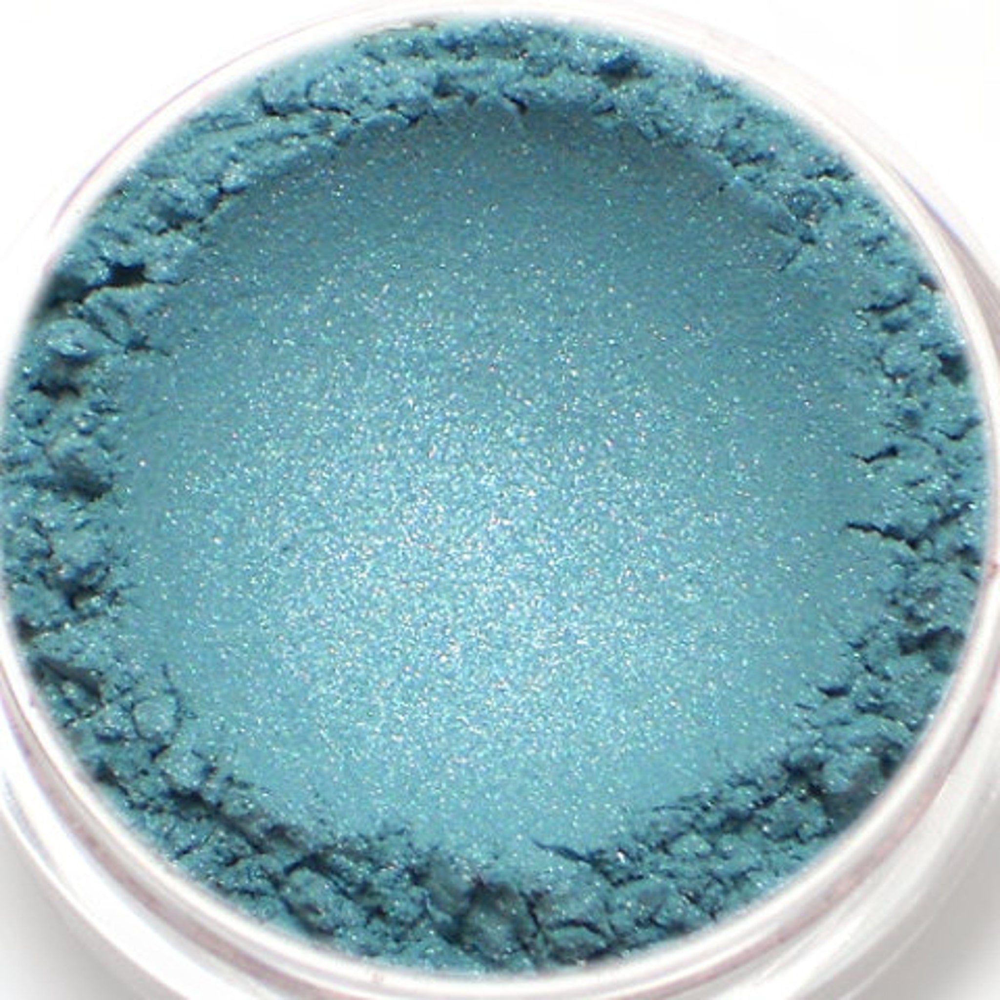 Close-up of shimmering frosty aqua blue mineral eyeshadow with sparkling flecks in compact pan