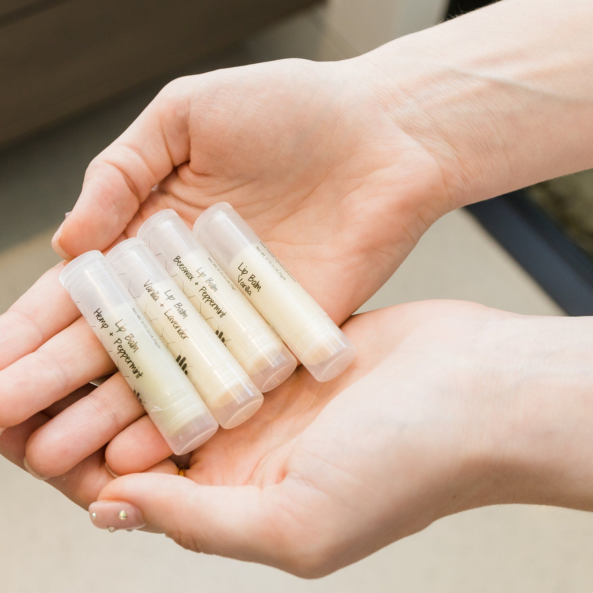 Lip balms in clear tubes, held in hands, with HandCraft Skincare branding visible on labels