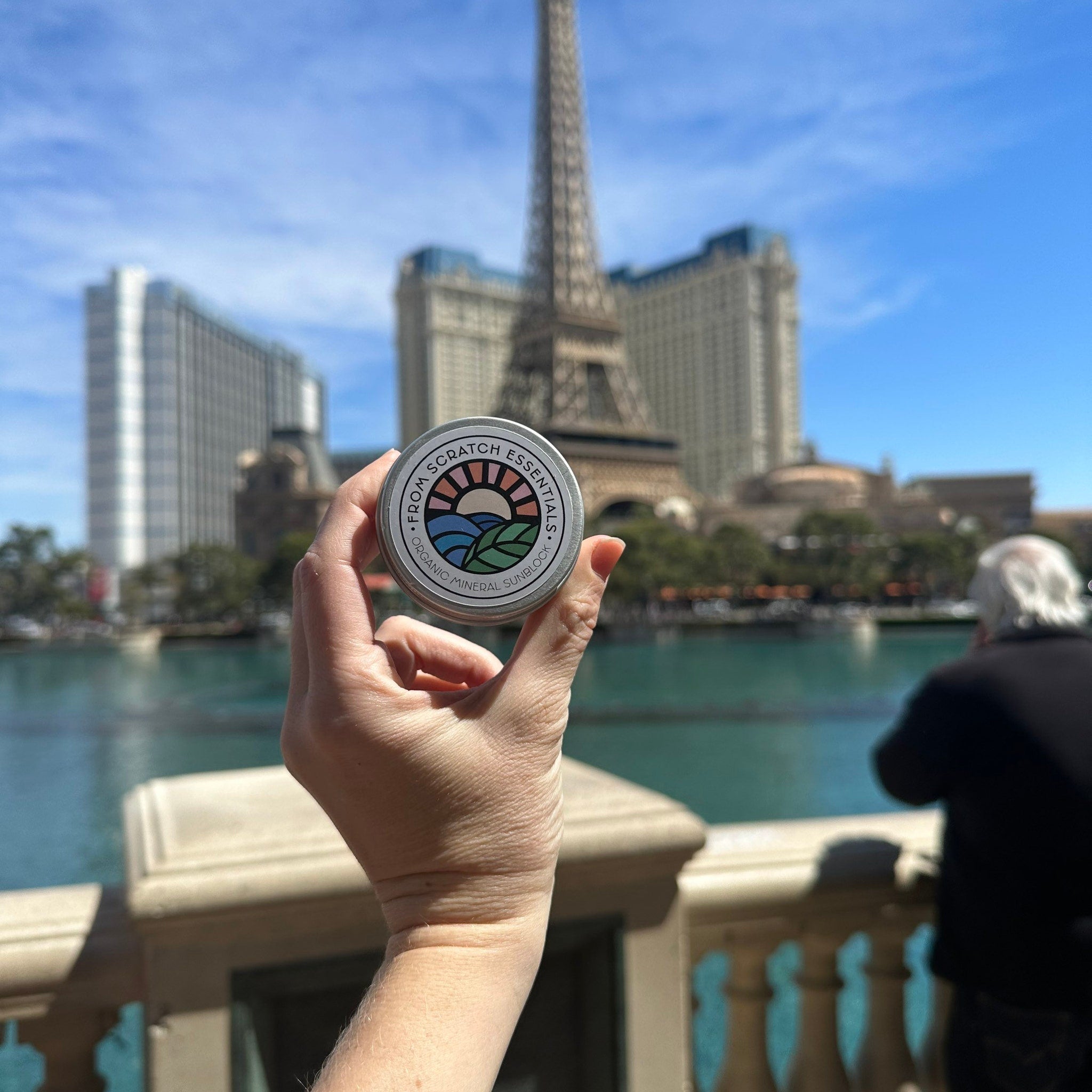 Sunblock tin with From Scratch Essentials logo, silver metal container, held in hand outdoors