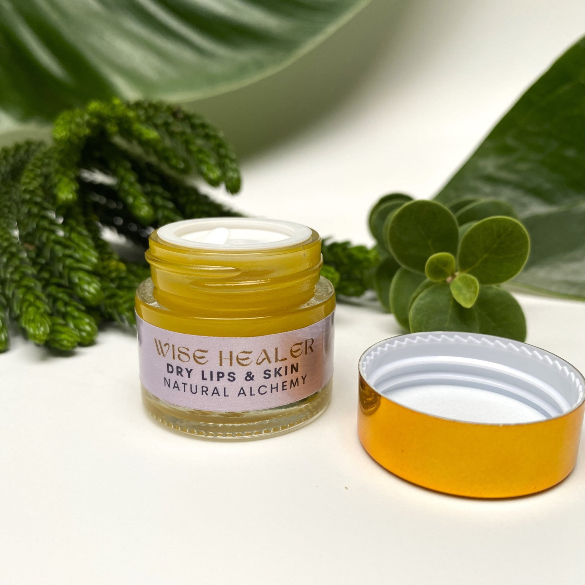 Lip balm jar with yellow liquid, gold lid, and "Wise Healer" label visible