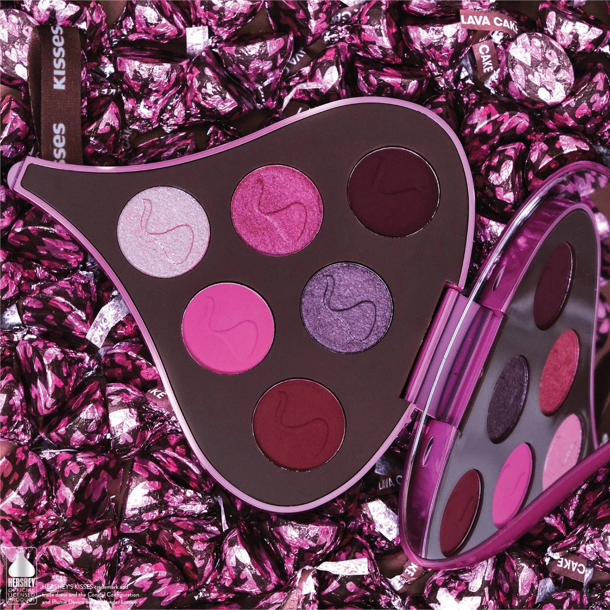 Eyeshadow palette with pink, purple, and brown shades in a heart-shaped compact, surrounded by pink foil candy wrappers
