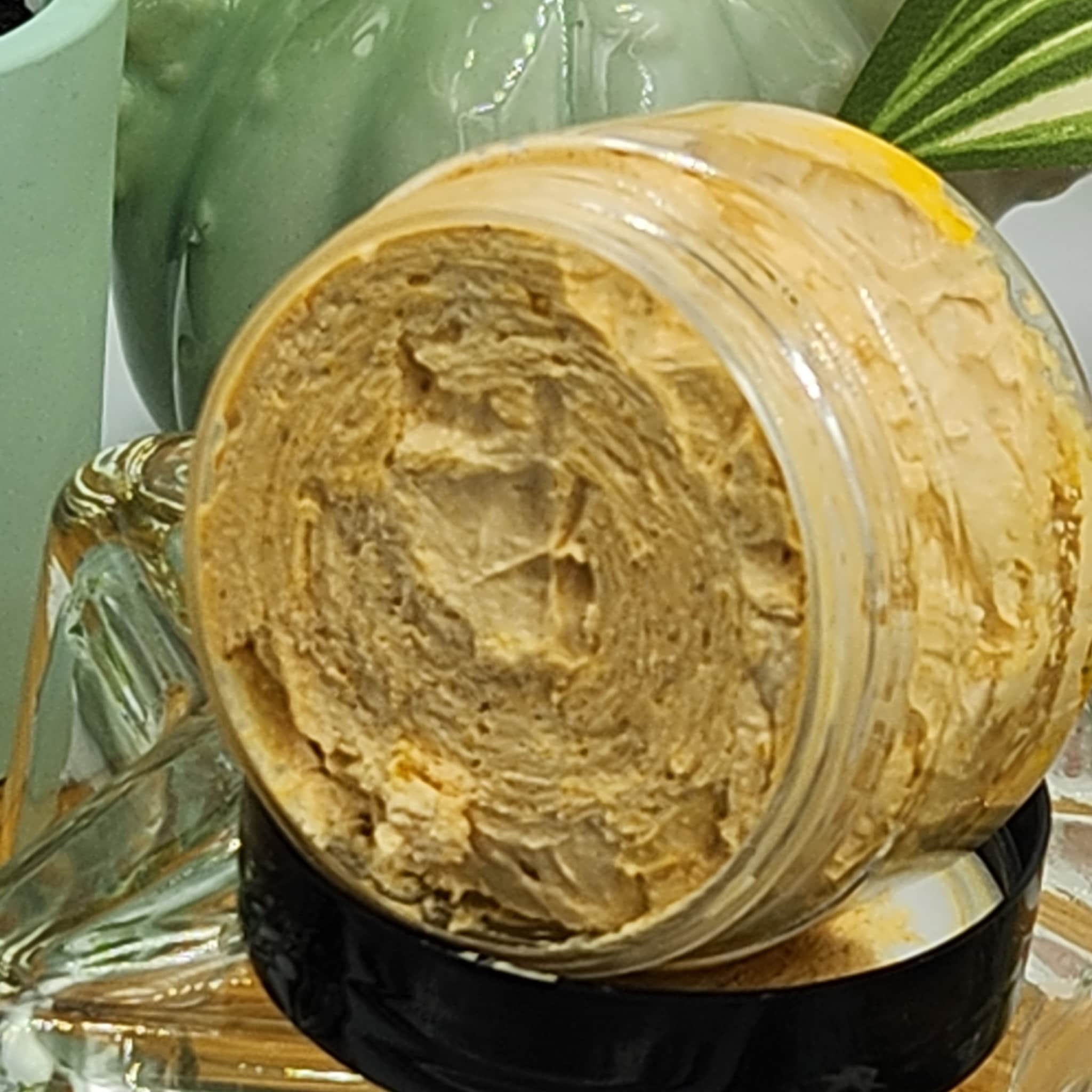 Jar of tan cream with visible texture inside a clear plastic container with black lid