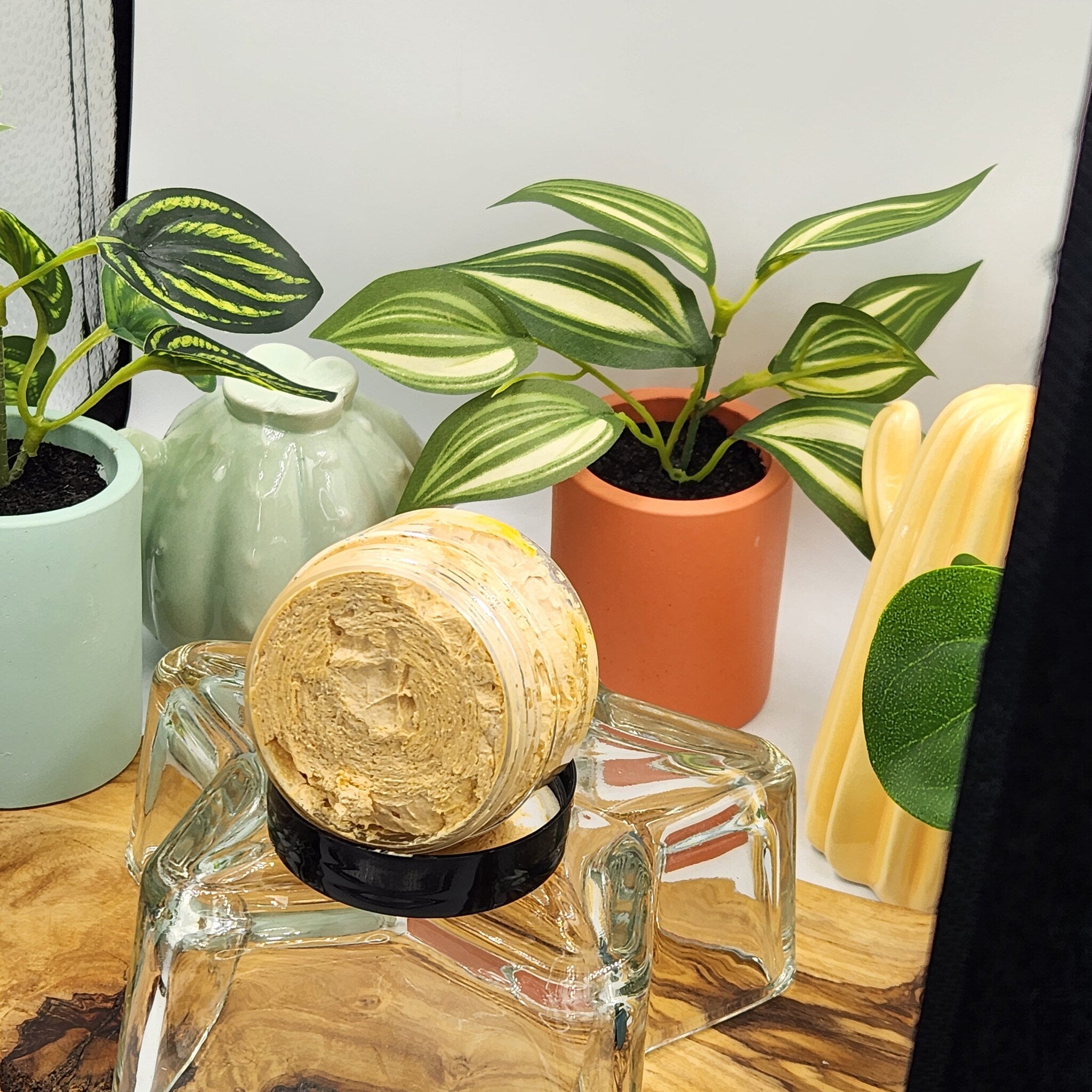 Cream jar with tan cream, black lid, and clear glass cube on wooden surface