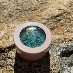 Hand applying emerald green shimmer eyeshadow with fingertip onto eyelid for bold look