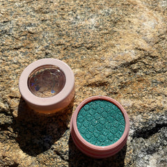 Eye shadow, teal green with scale pattern, in pink compact, open and closed on rock surface