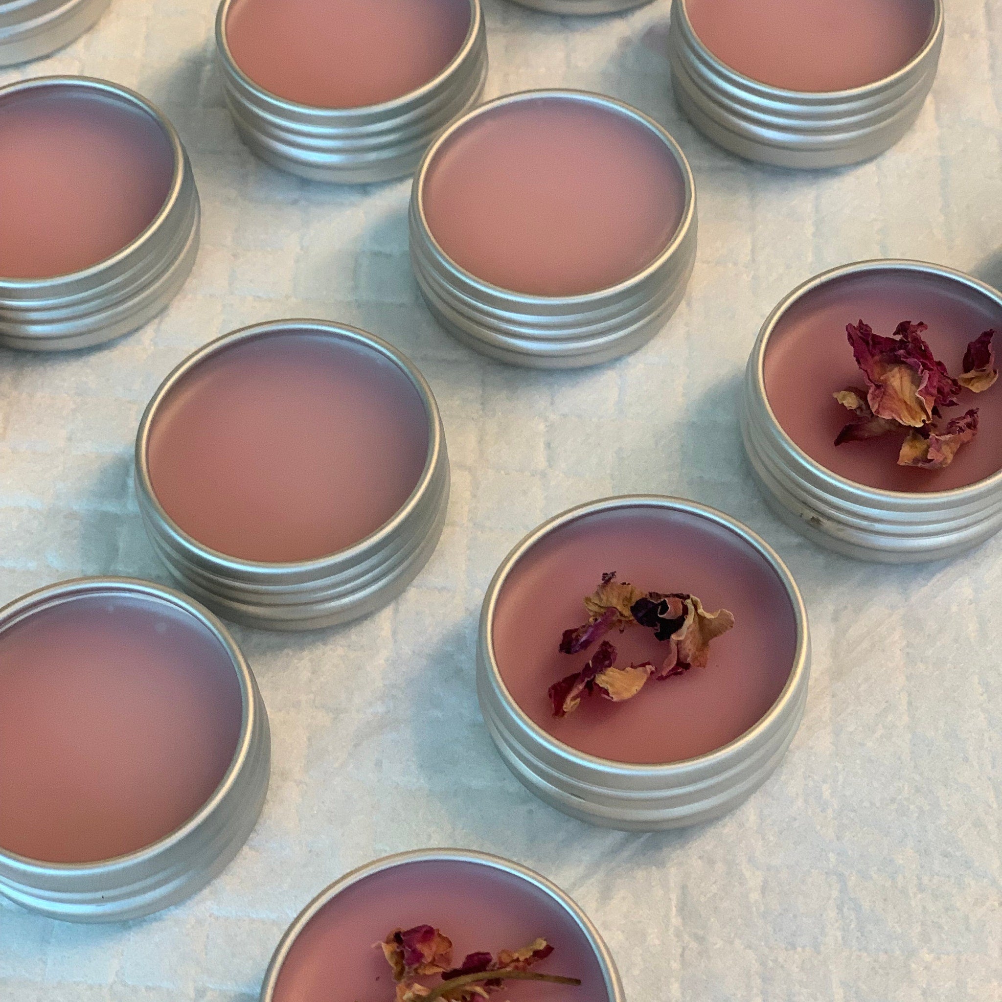 Lip balm in silver tins with pink balm and dried rose petals on white surface