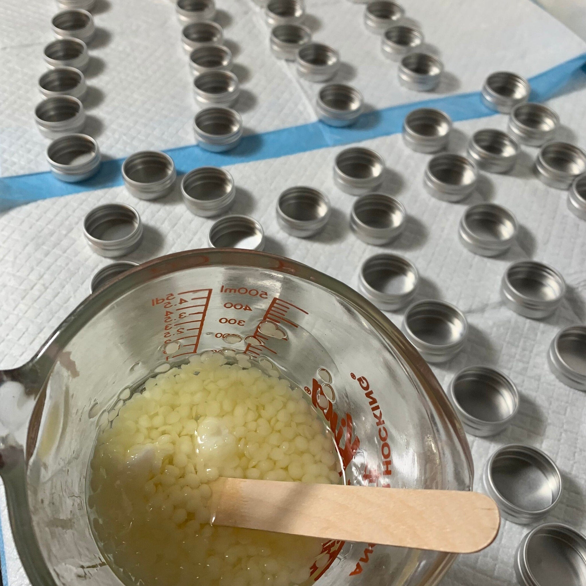 Metal lip balm tins, silver metal, arranged on white surface, with measuring cup and ingredients