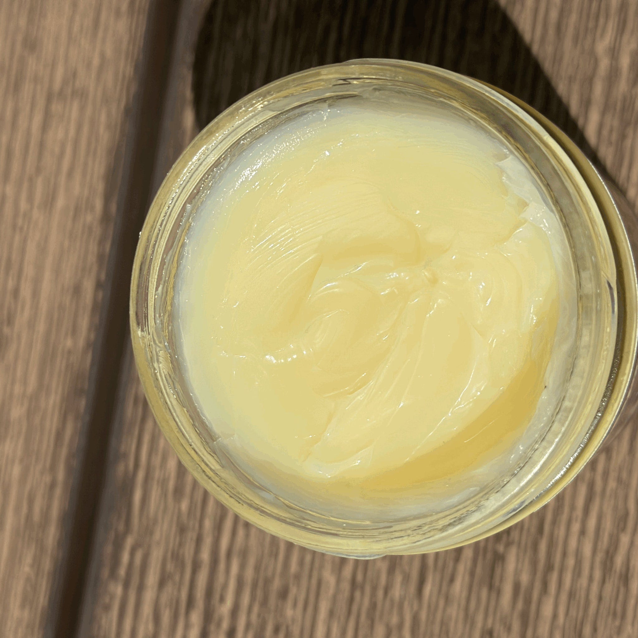 Yellow ointment in a clear glass jar, on a wooden surface, with visible texture.