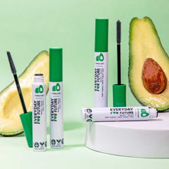 Mascara tubes with green caps and white labels, black mascara wands, and avocado slices