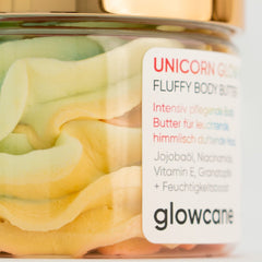 Hand applying unicorn glow body butter from a white jar onto smooth skin, showing rich texture