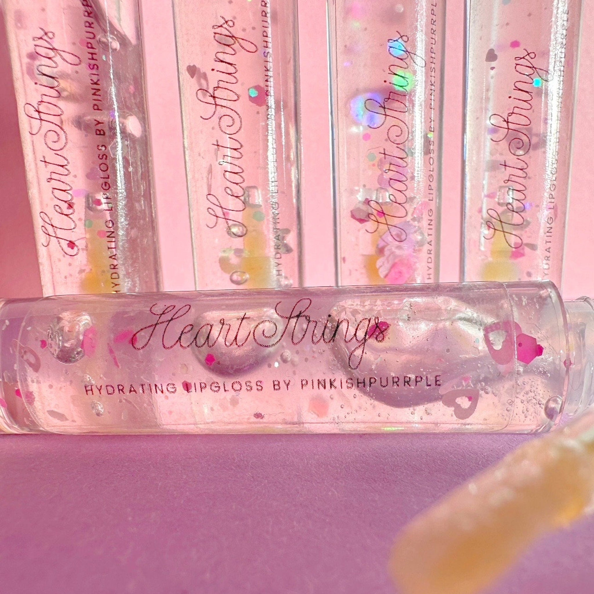 Lipgloss with pink glitter, clear tube, and "Heart Strings" text on pink background