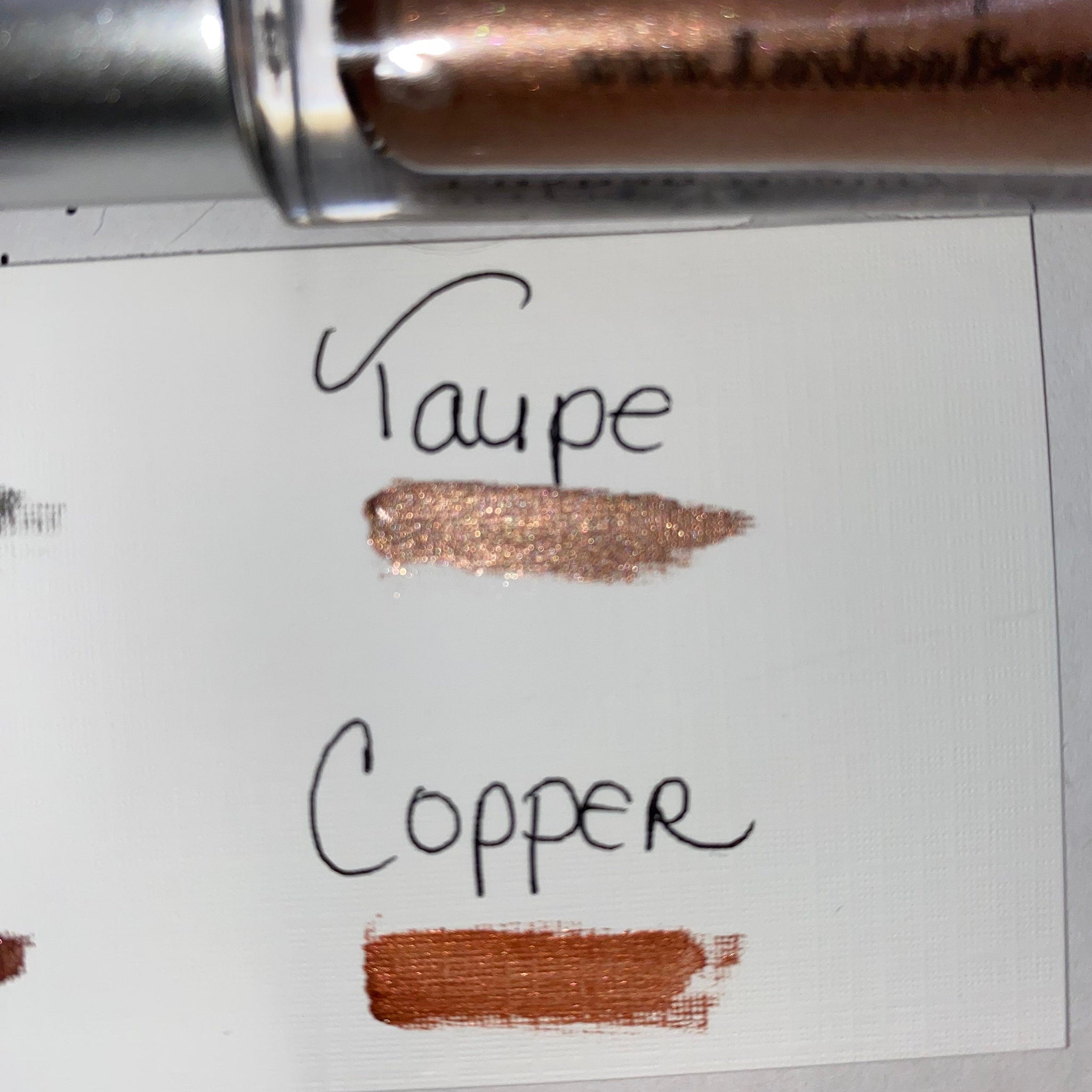 Makeup swatches of taupe and copper metallic color on white paper